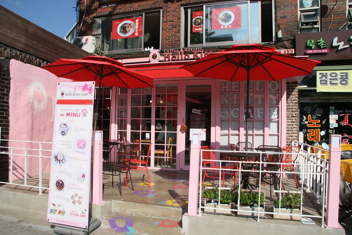 Pink Hello Kitty Cafe exterior with red umbrellas over outdoor seating.