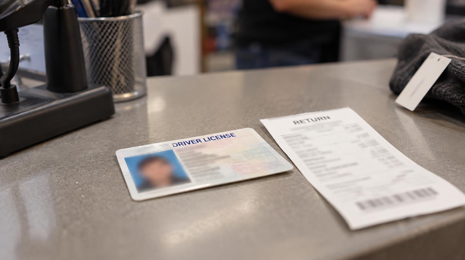 A driver's license lying on a retail counter next to a return receipt.