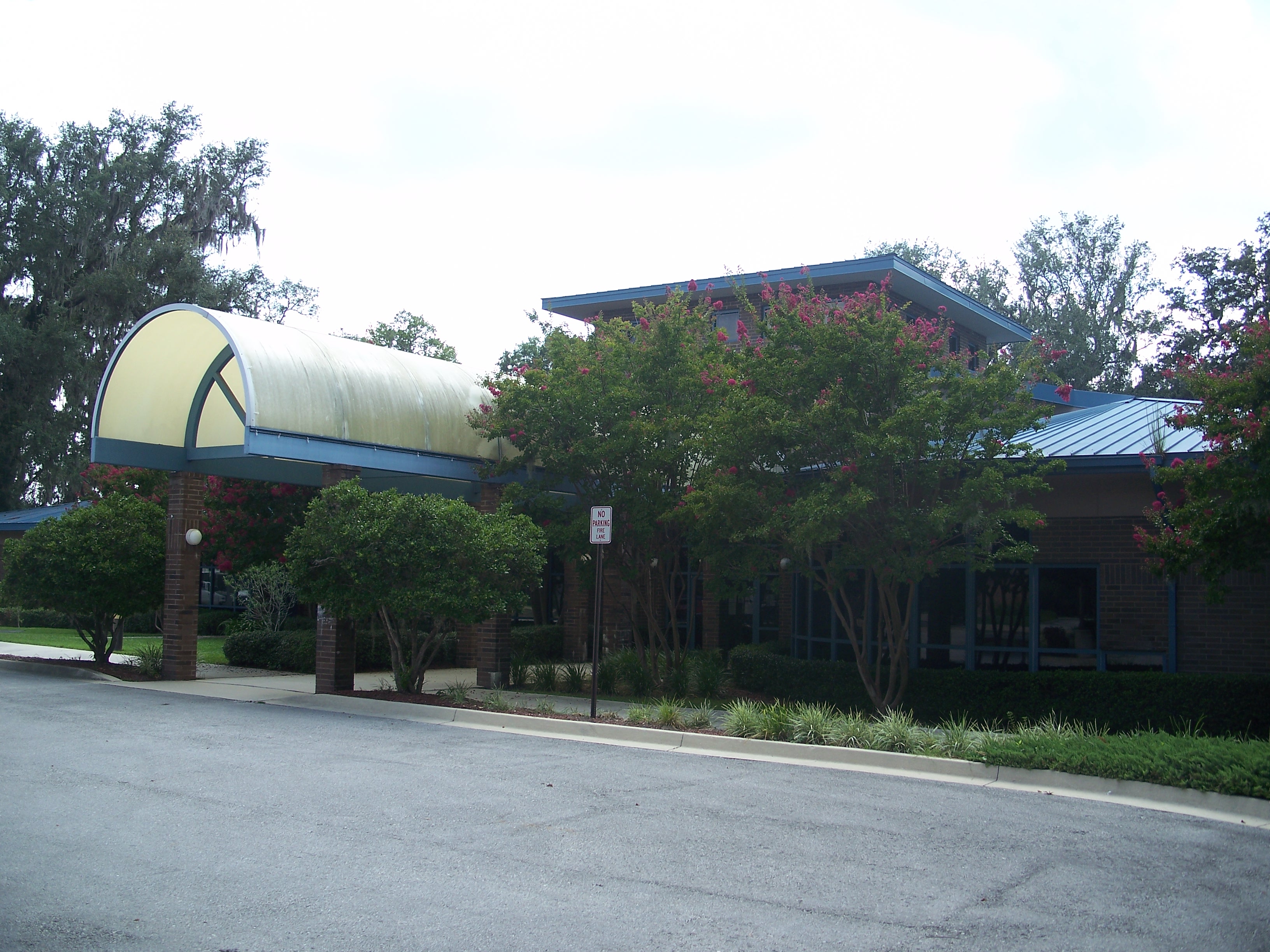 Single-story brick municipal building with curved colorful canopy entrance viewed from a parking lot.