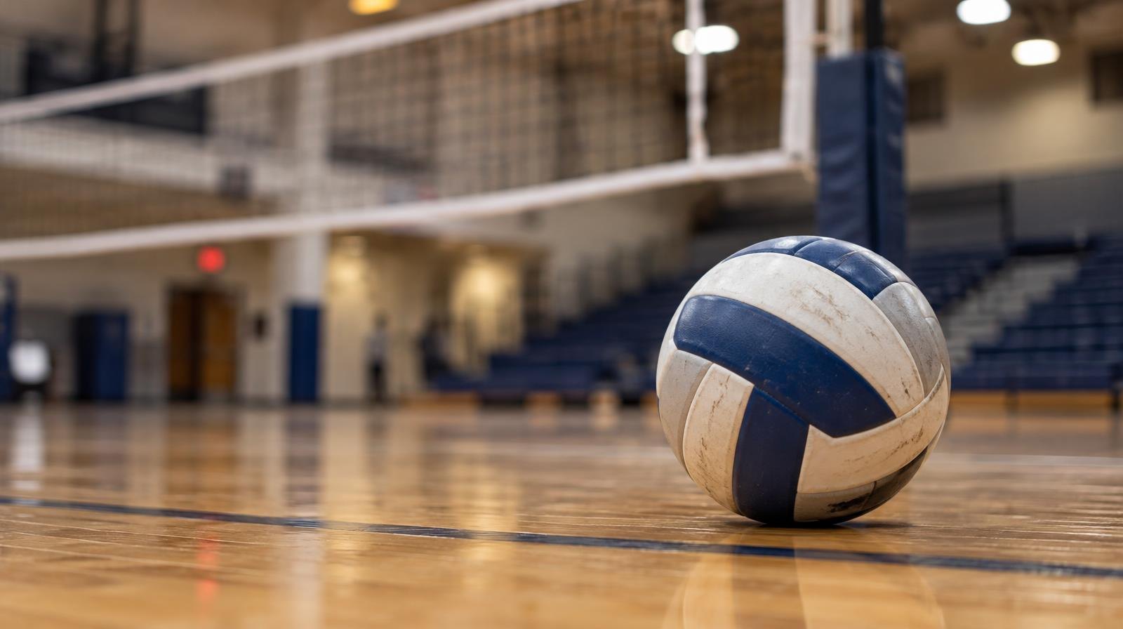 A volleyball resting on a hardwood gym floor near a net.