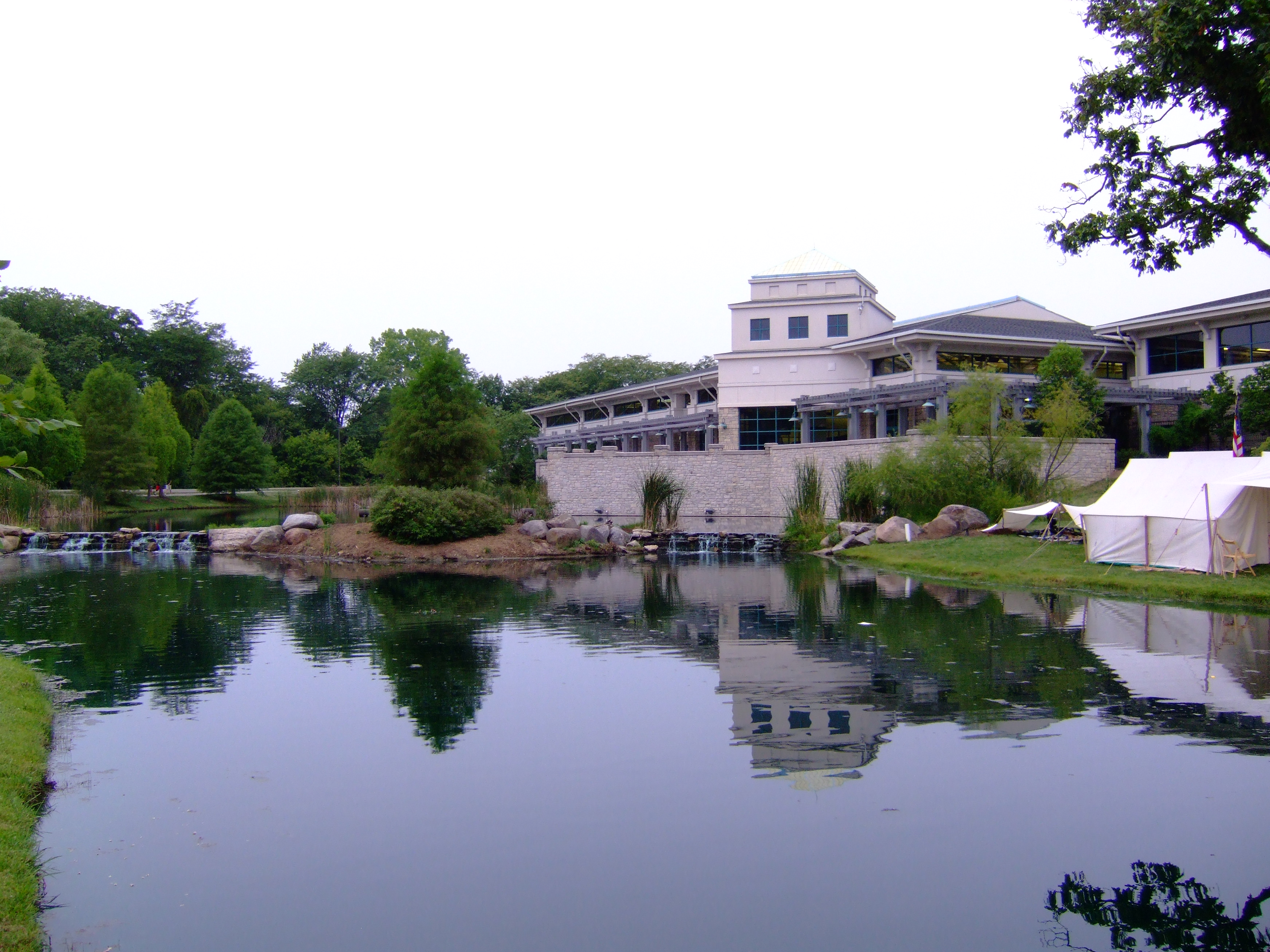Modern recreation center building reflected in a calm pond, surrounded by trees.