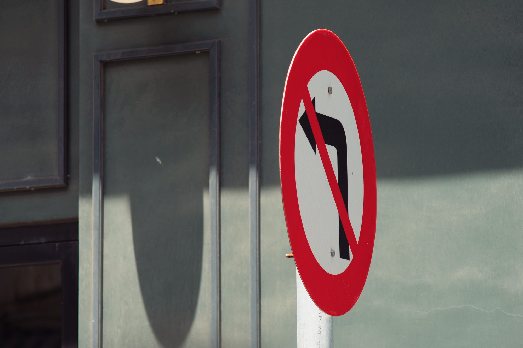 A no left turn road sign displayed prominently in an urban setting against a building background.