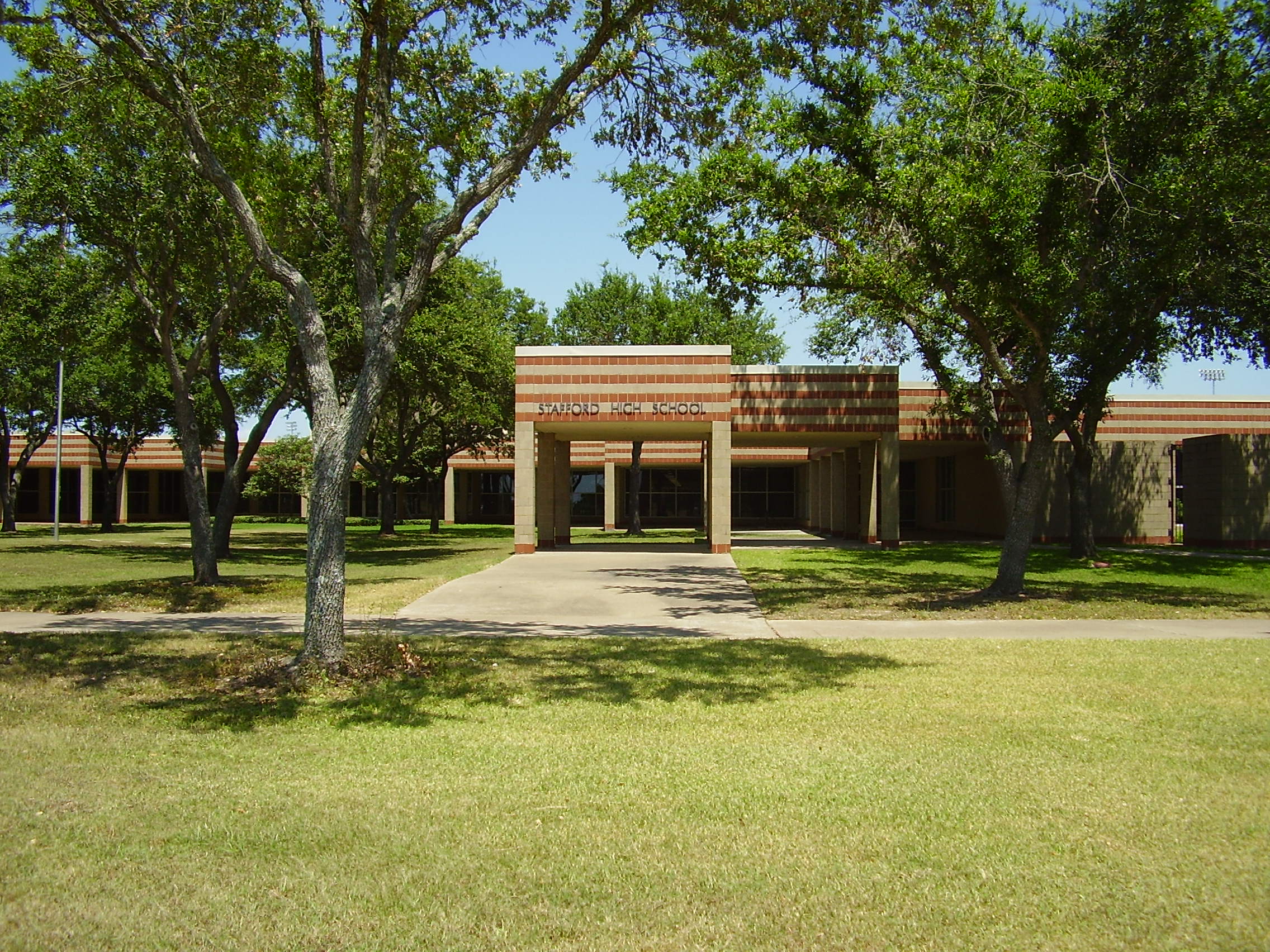Exterior of a single-story brick school building with a covered entrance and mature trees.