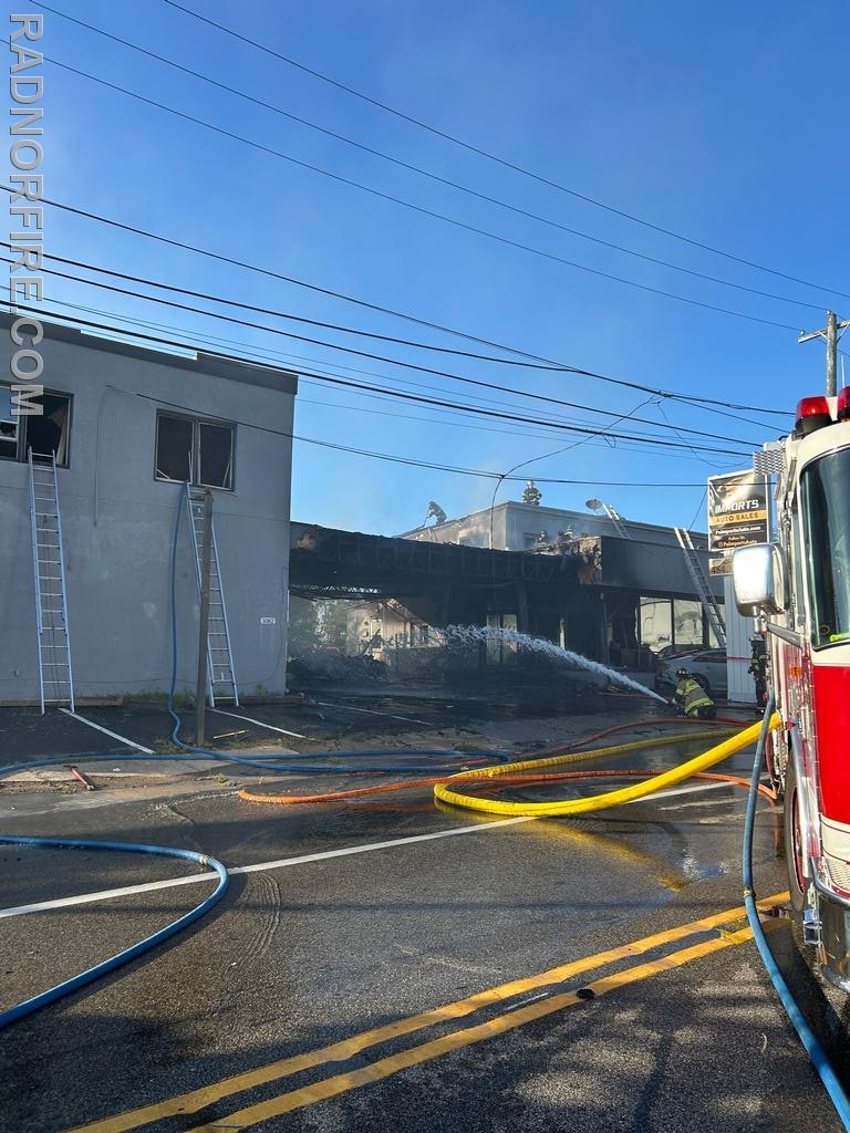 Firefighters aim hoses at a fire-damaged commercial building with a collapsed roof.
