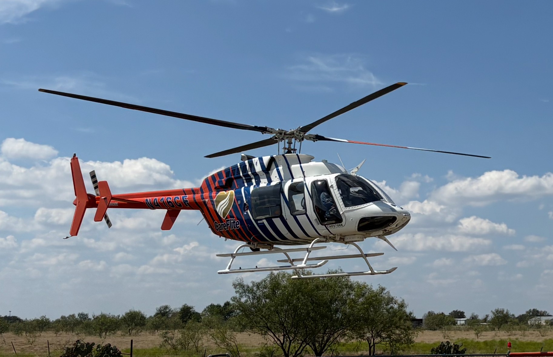 A red, white, and blue Care-Flite helicopter flying low over trees.