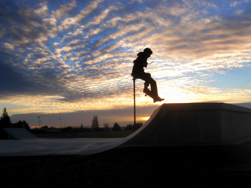 Silhouette of a skateboarder airborne above a concrete ramp at sunset.