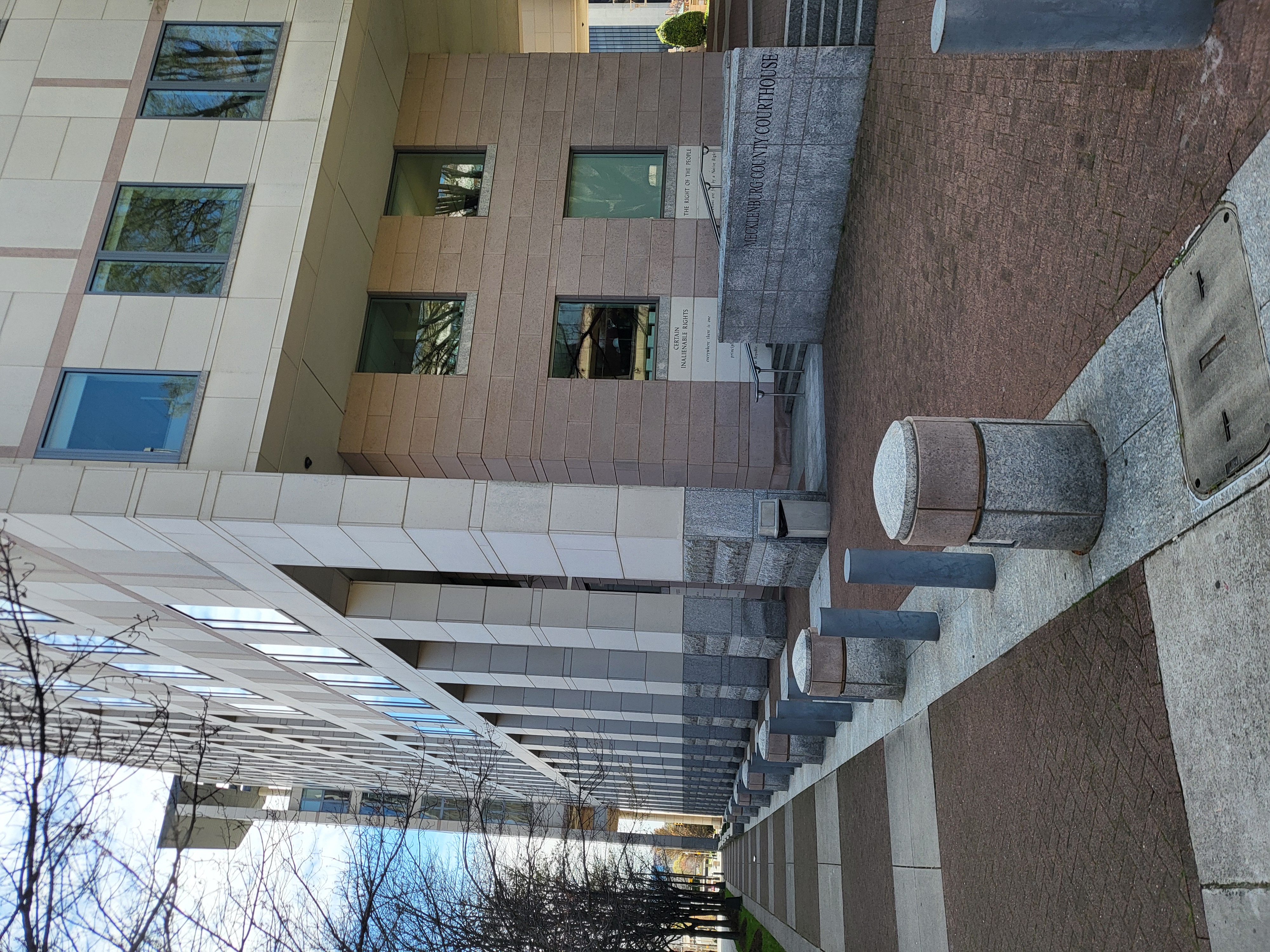 Exterior of the Mecklenburg County Courthouse building with a sign and security bollards.
