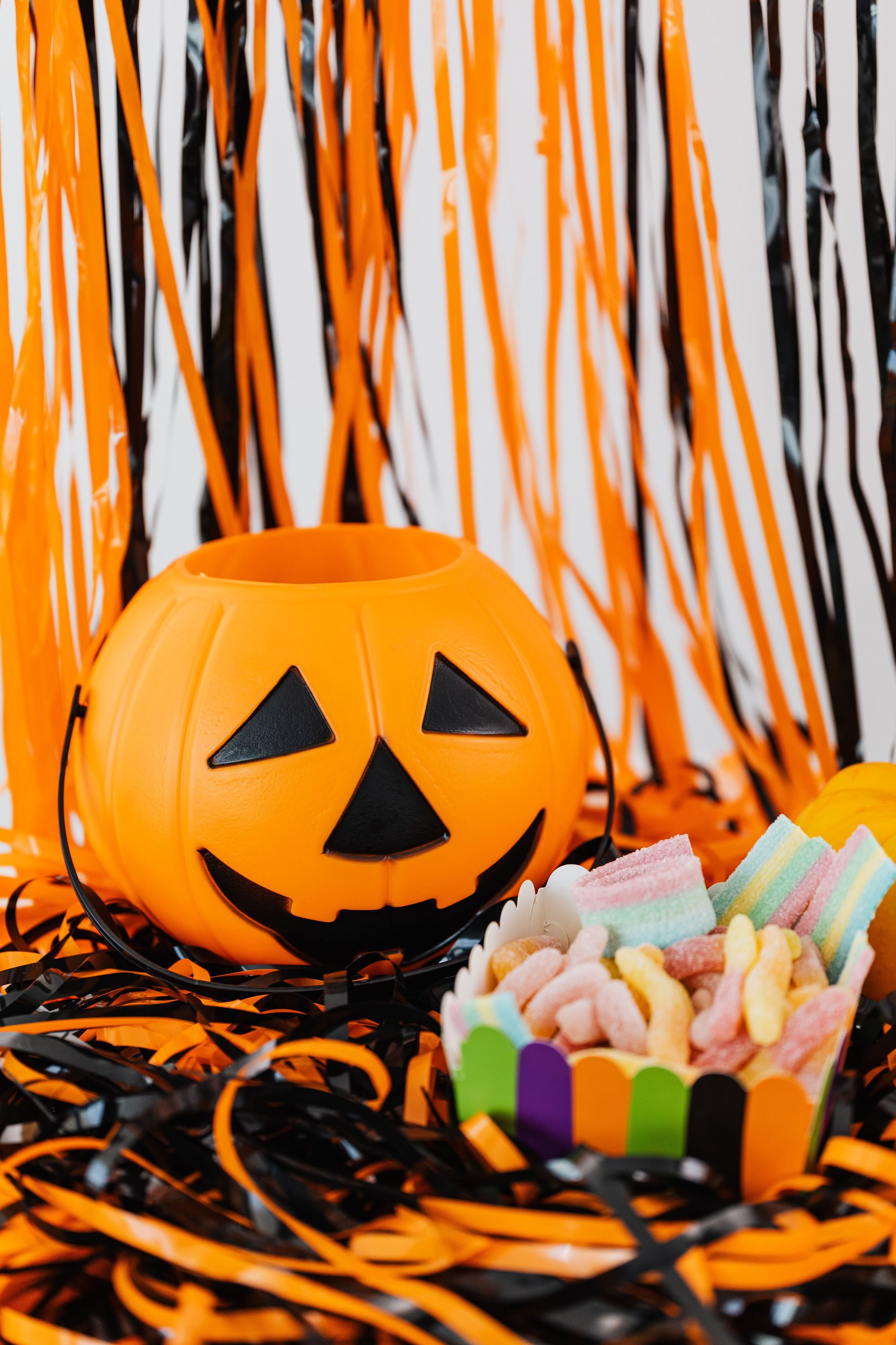 Colorful Halloween candies beside a pumpkin bucket with festive streamers.