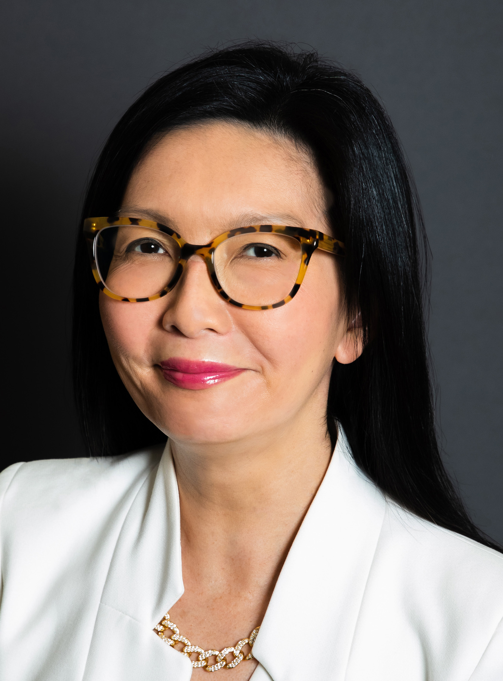 Woman in white blazer and tortoiseshell glasses poses for a professional portrait.