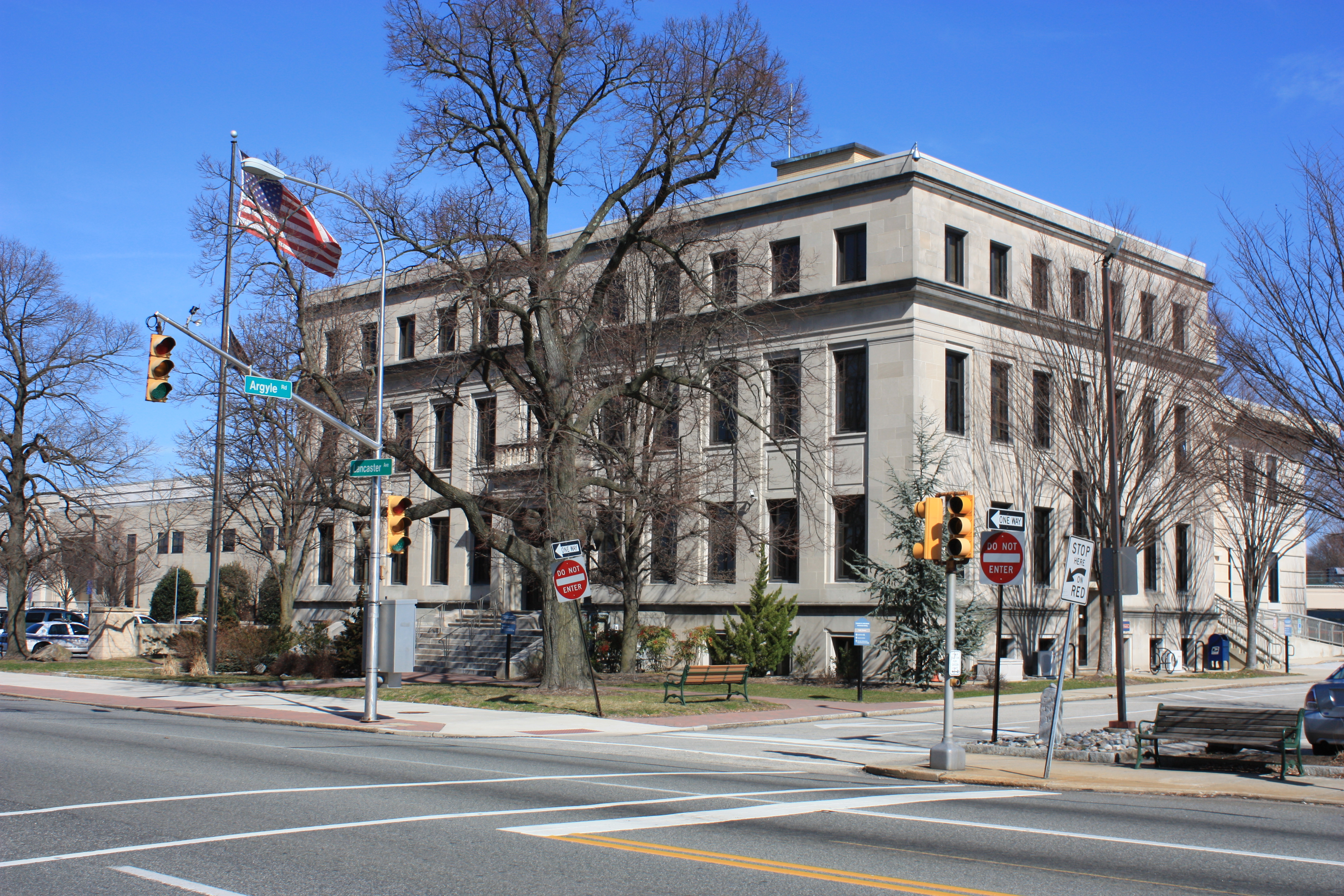 Large neoclassical stone building at a street corner with an American flag and traffic signals.