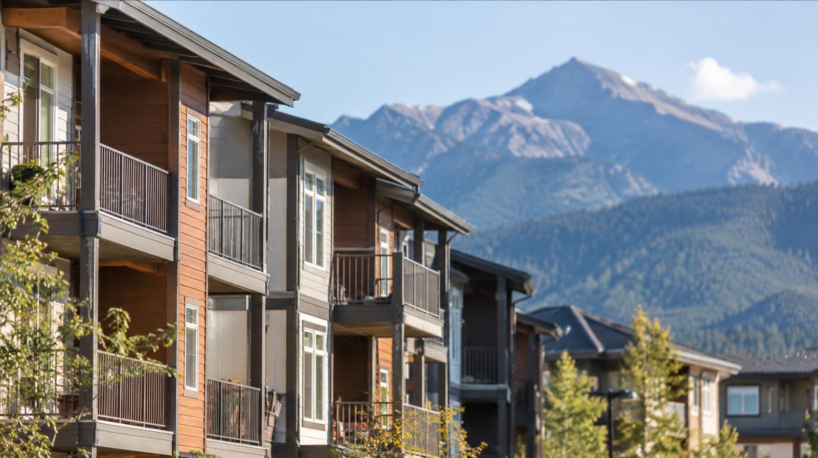 A row of modest apartment buildings with snow-capped mountains behind them.