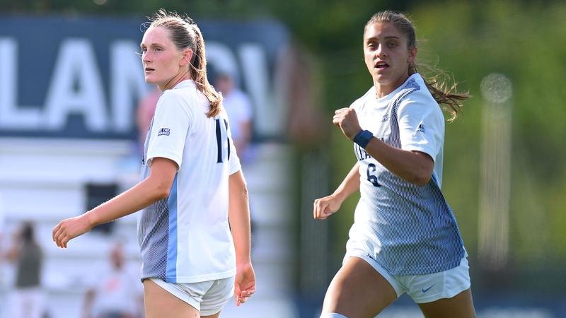 Two female soccer players in light blue and white uniforms on a grass field.