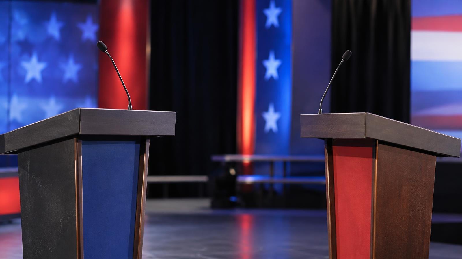 Two empty podiums on a stage illuminated by bright studio lights.