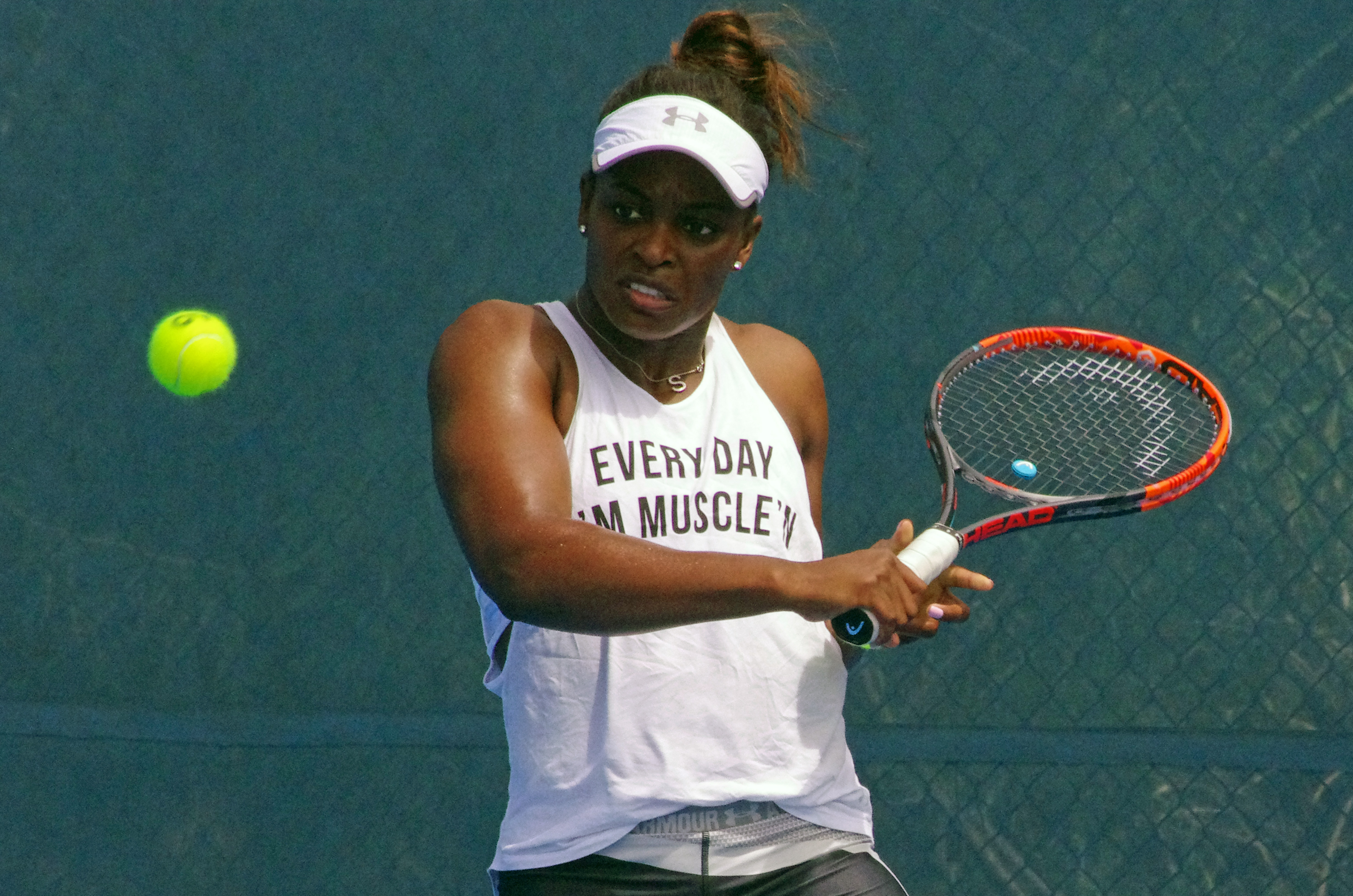 Tennis player hitting a two-handed backhand on an outdoor hard court.