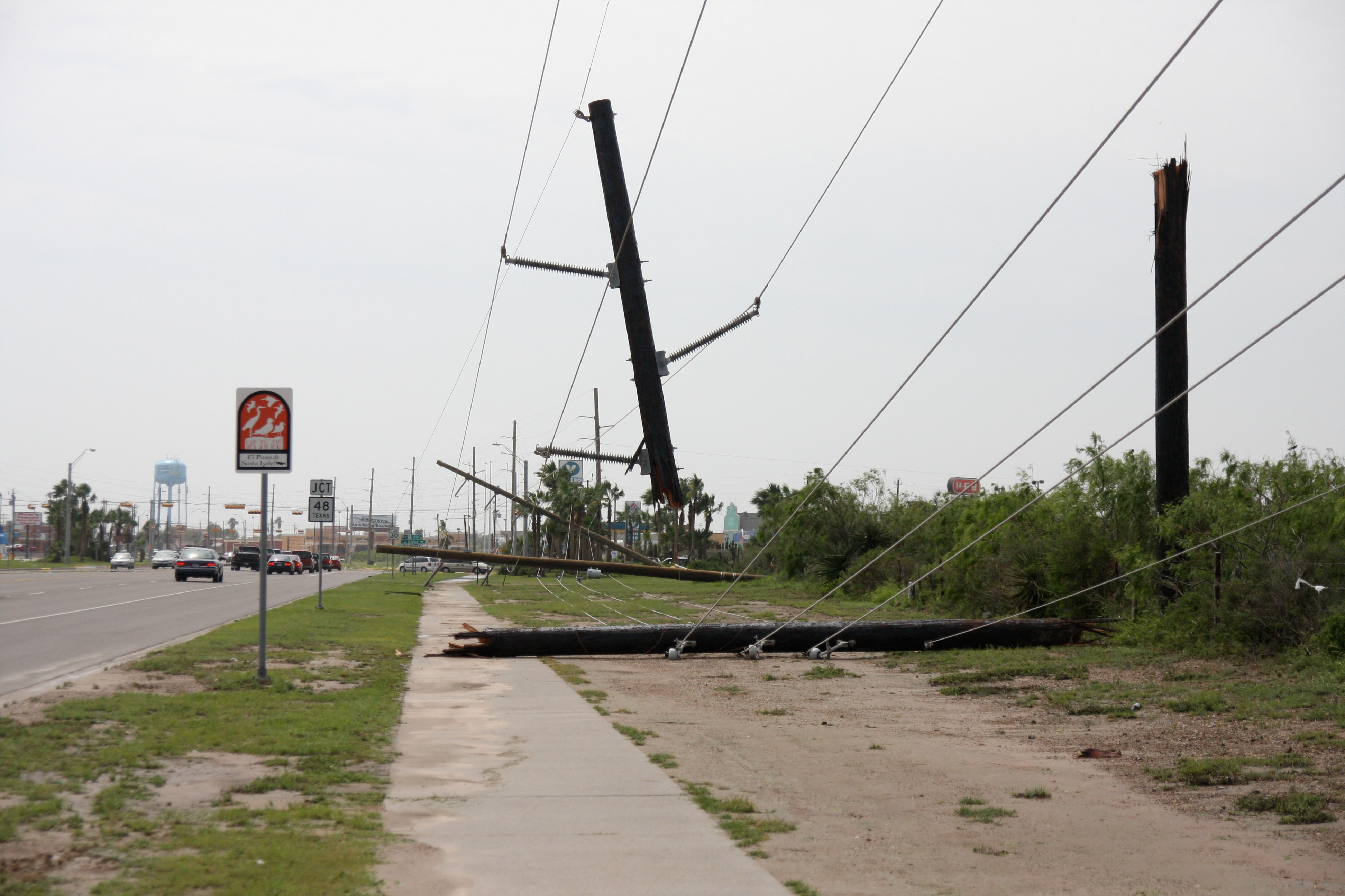 Multiple fallen utility poles with downed power lines along a roadway after a storm.