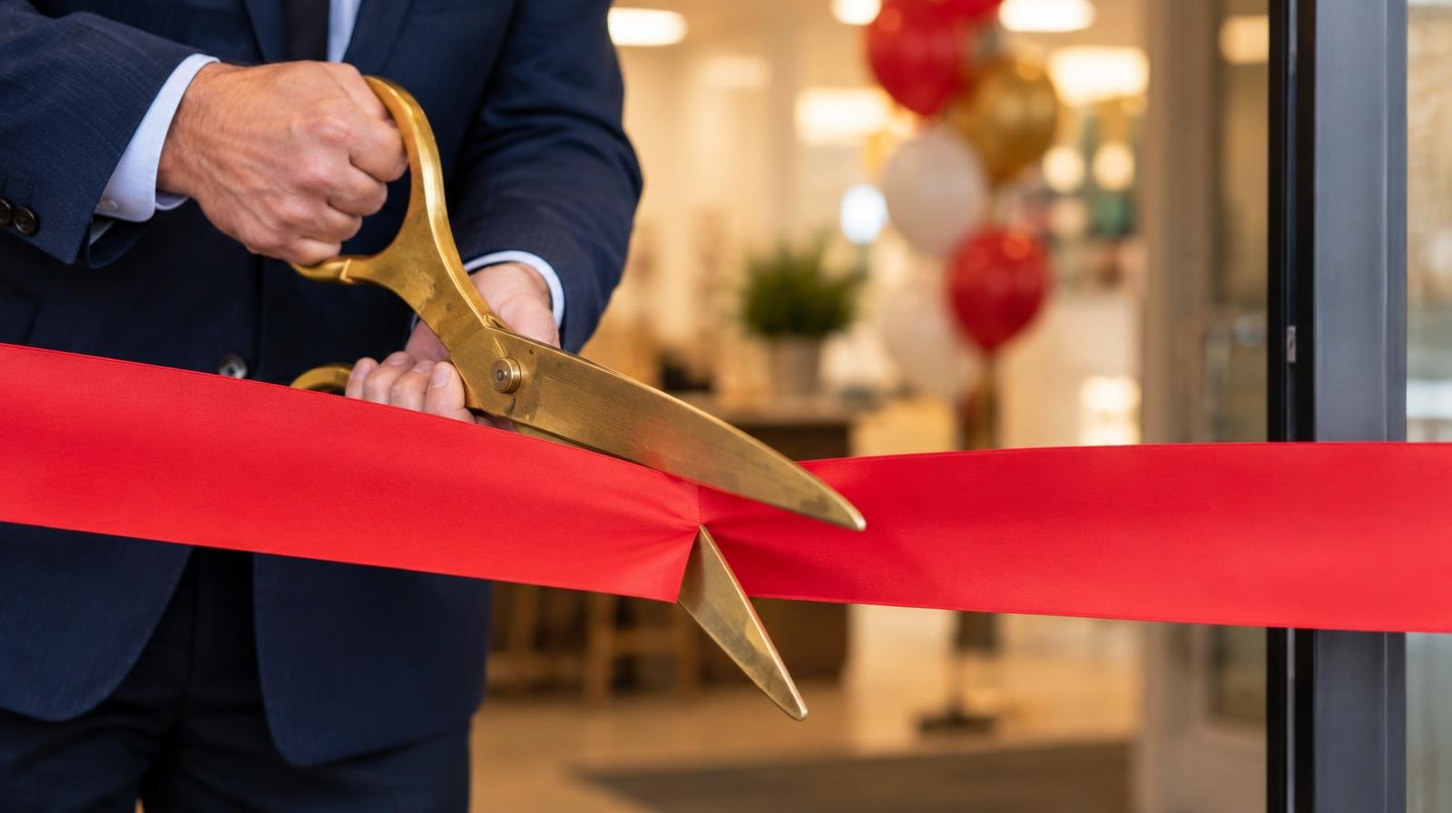 Ceremonial scissors cutting a bright red ribbon stretched across a doorway.
