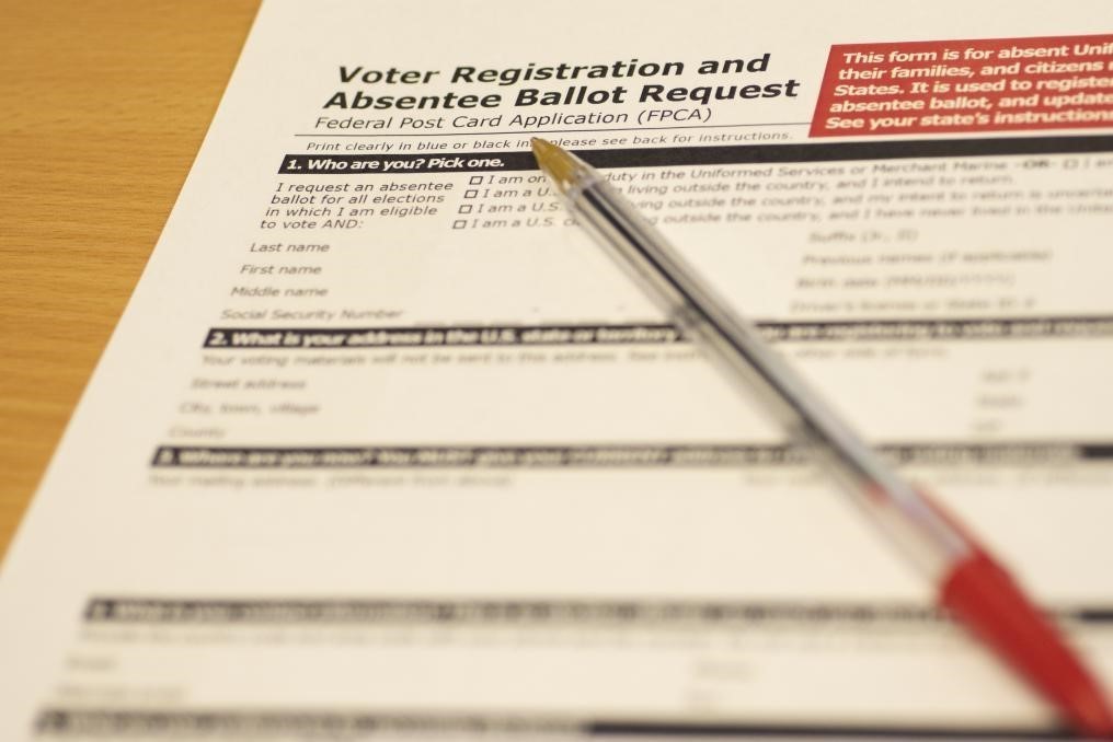 A voter registration and absentee ballot request form on a wooden surface with a red pen on top.