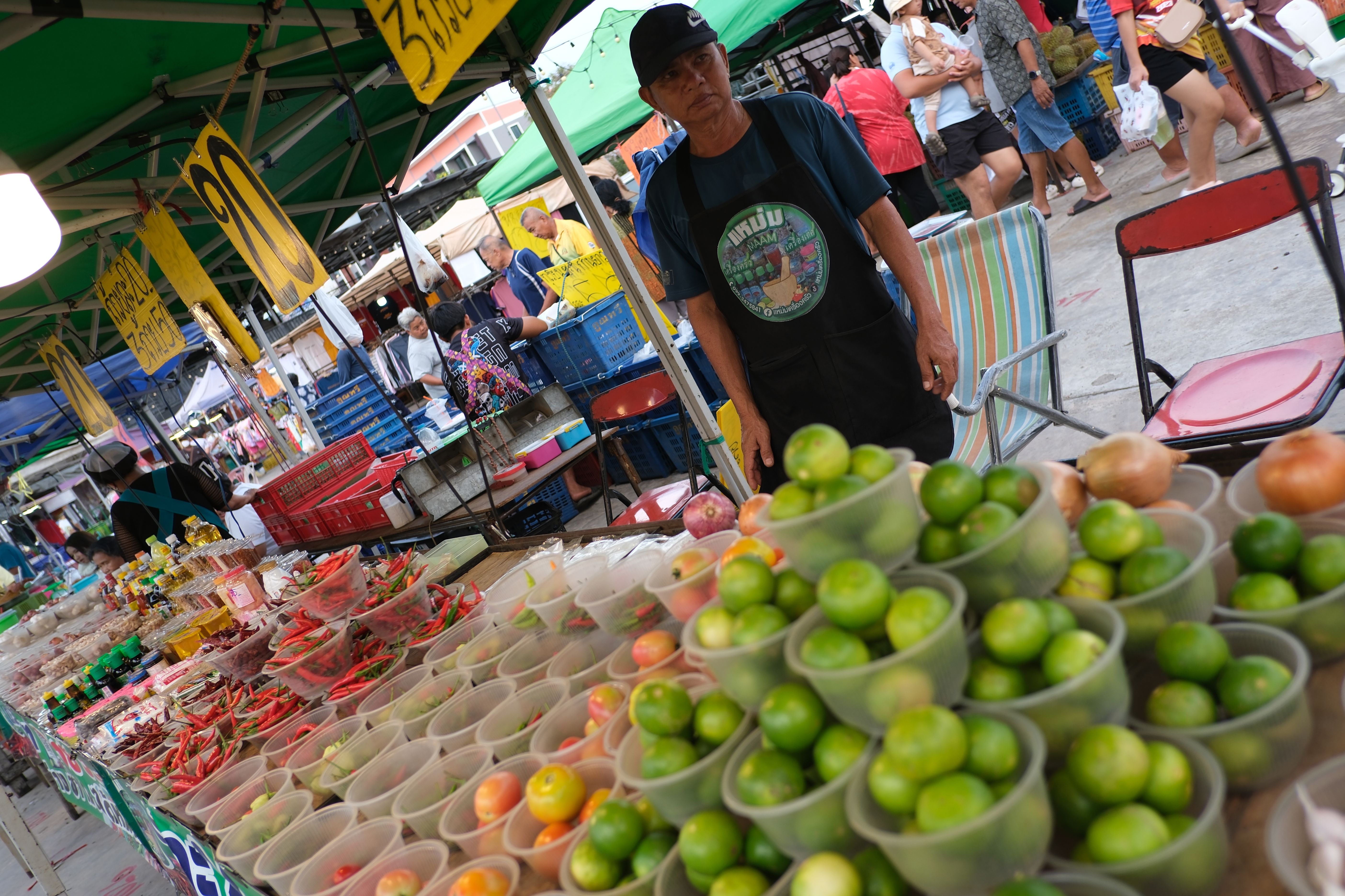 Vendor behind a market stall filled with cups of fresh limes and produce.
