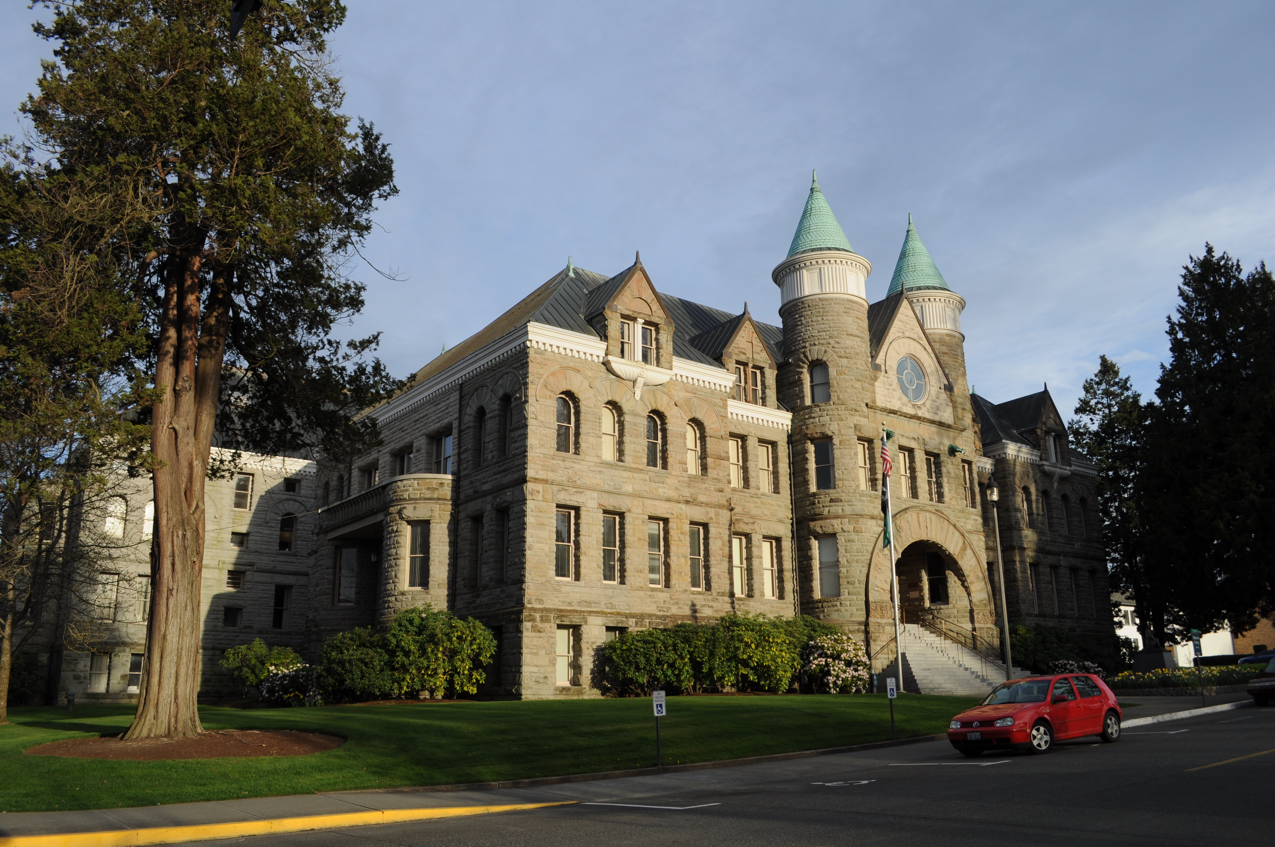 Historic stone building with turrets seen from a park on a sunny day.