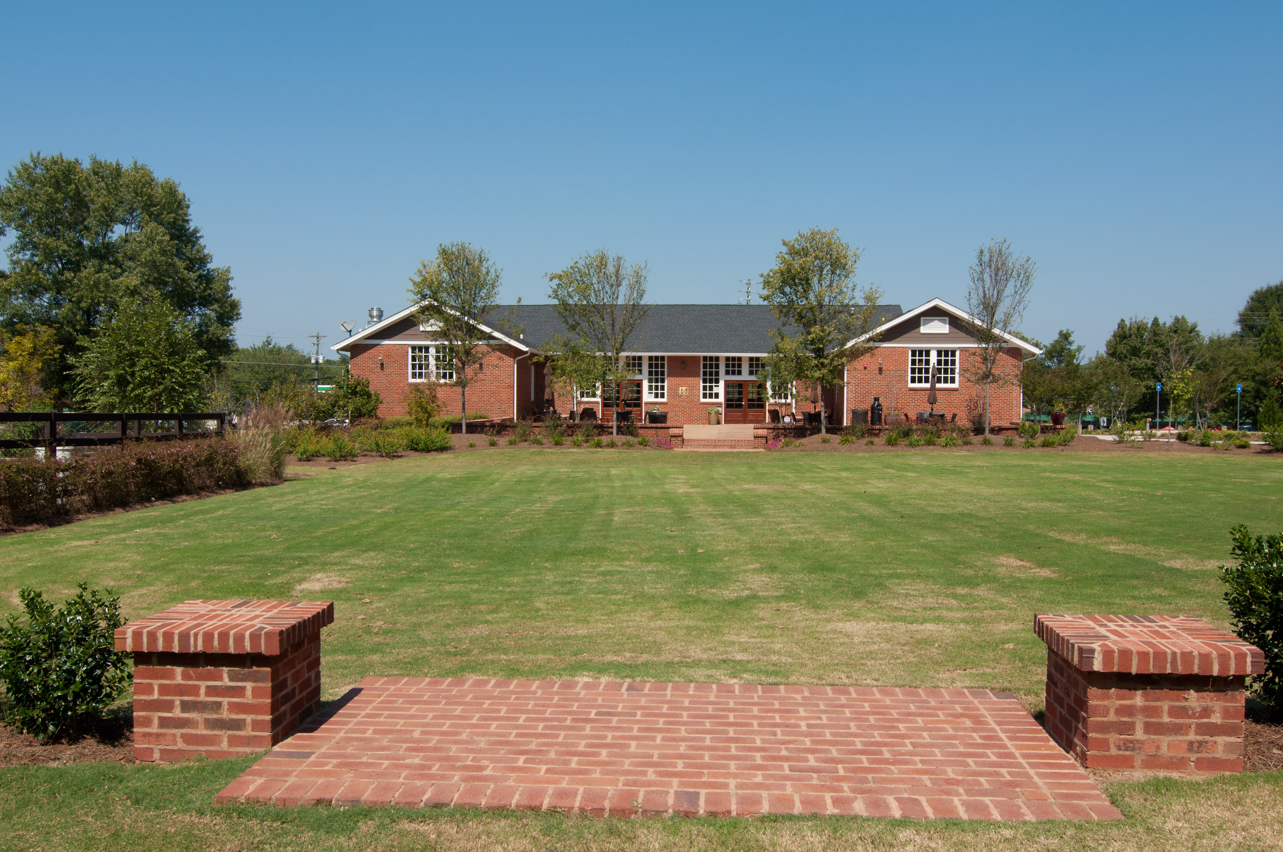 Single-story red brick school building set behind a wide green lawn under blue sky.