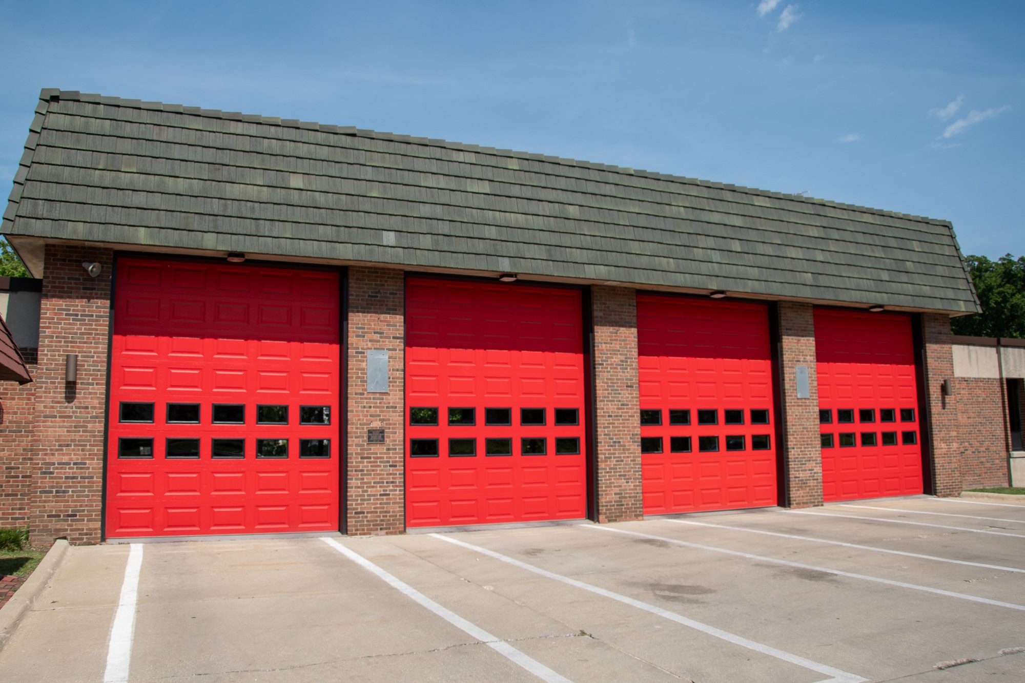 Brick fire station with four red overhead garage doors on a clear day.