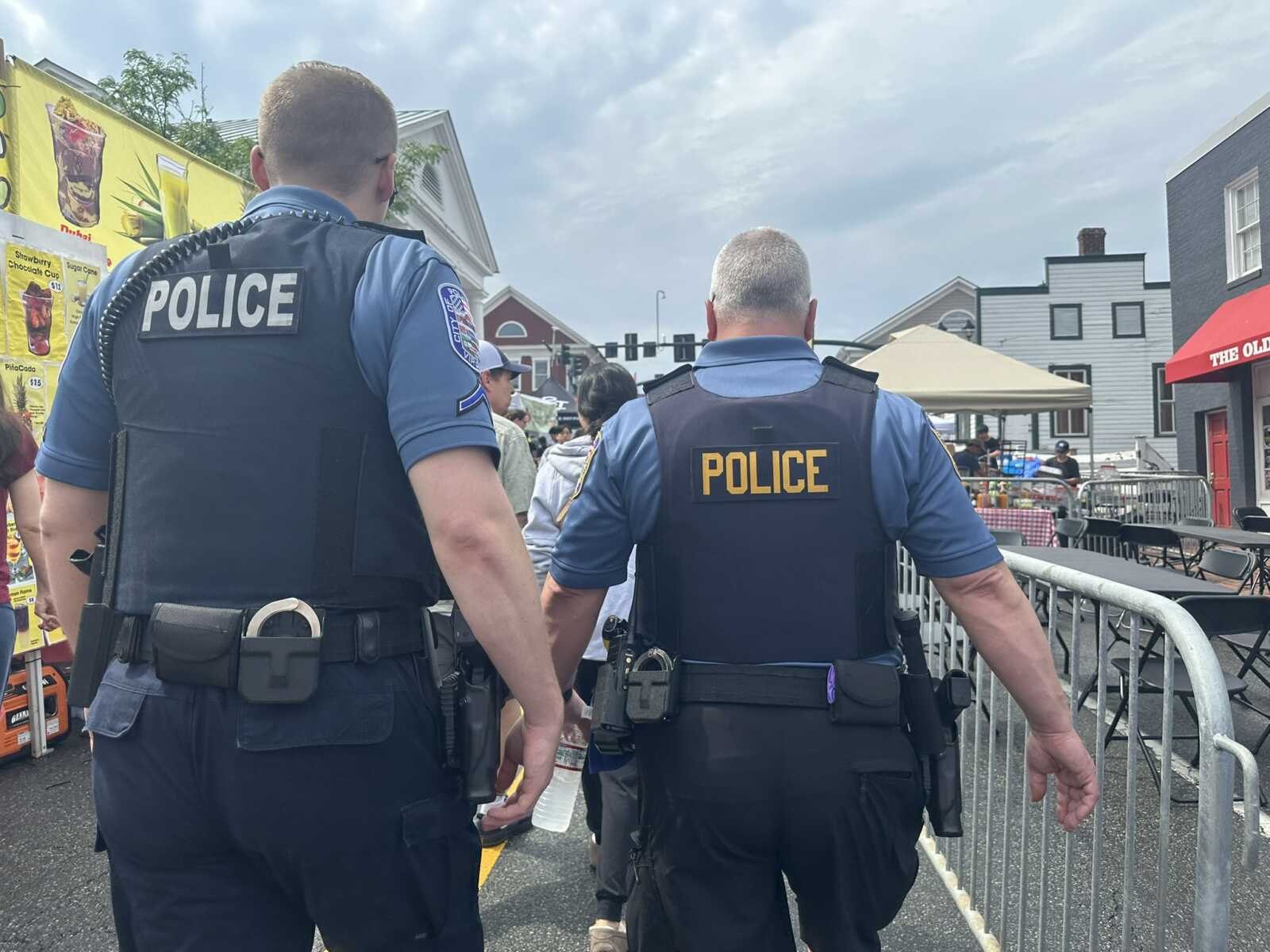 Two police officers in blue uniforms walking through a crowded outdoor festival, radios on their belts.