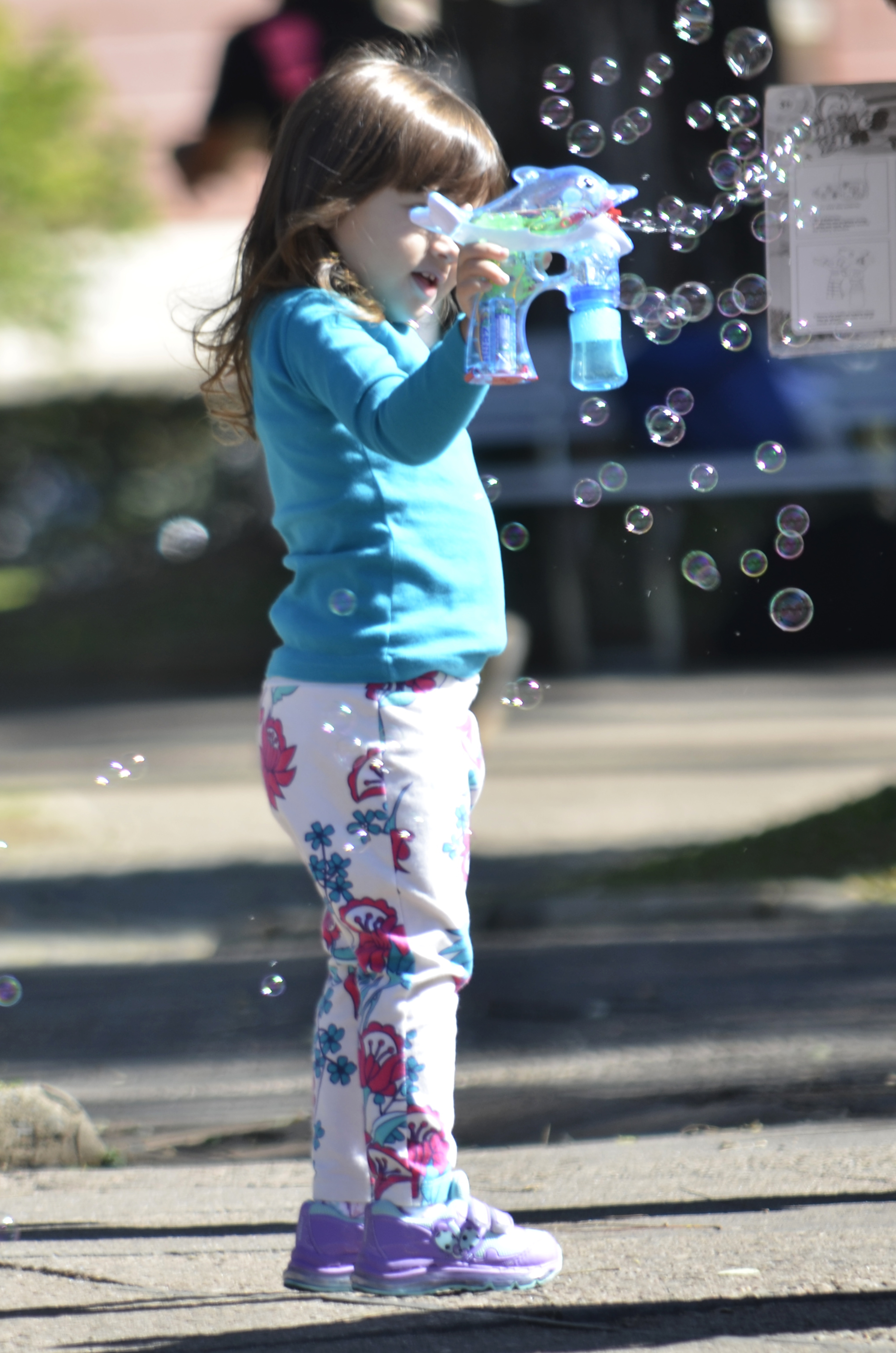 Young girl in teal top holds a bubble gun toy, surrounded by floating soap bubbles.