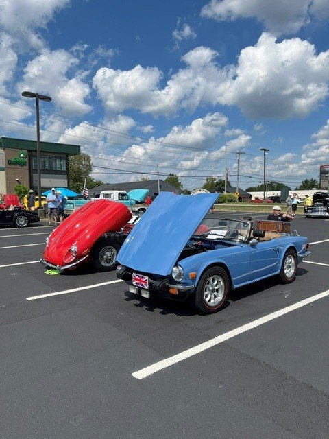 A blue vintage roadster with hood open and a red Volkswagen Beetle parked at an outdoor car show.