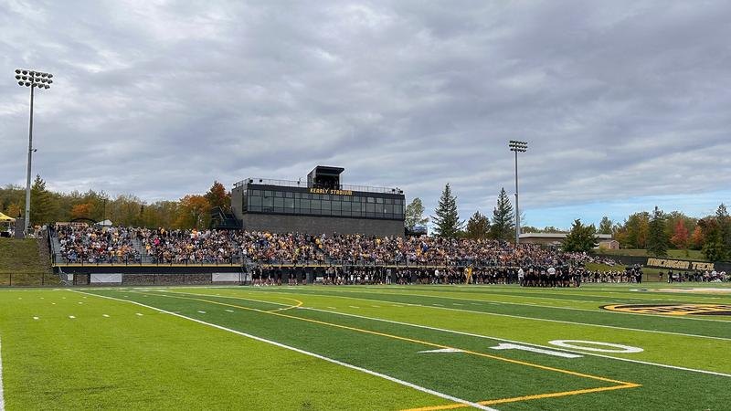 Football stadium grandstand filled with fans under an overcast sky.