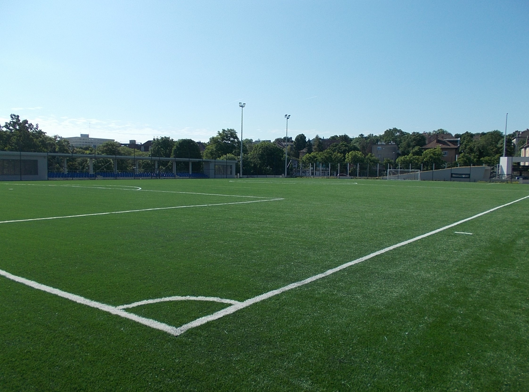 Empty artificial turf soccer field with white line markings under a clear blue sky.