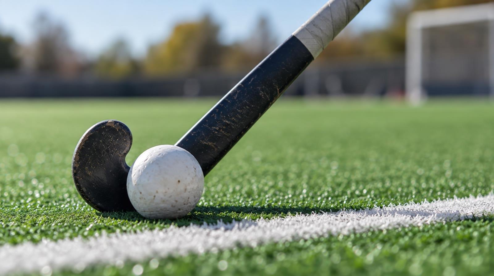 A field hockey stick and ball resting on green artificial turf near a white line.