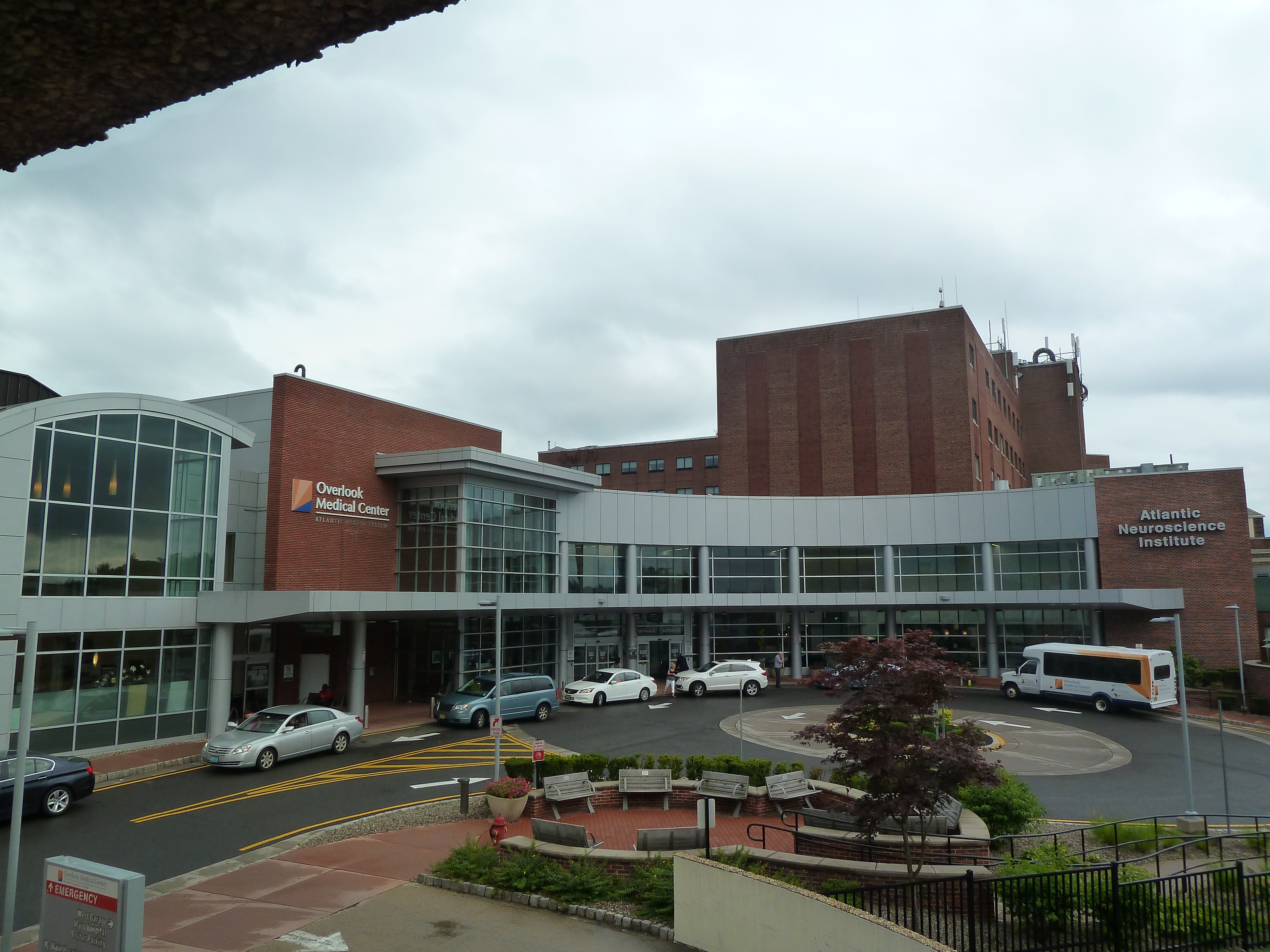 Exterior of a large brick hospital complex with a covered entrance and parked vehicles.