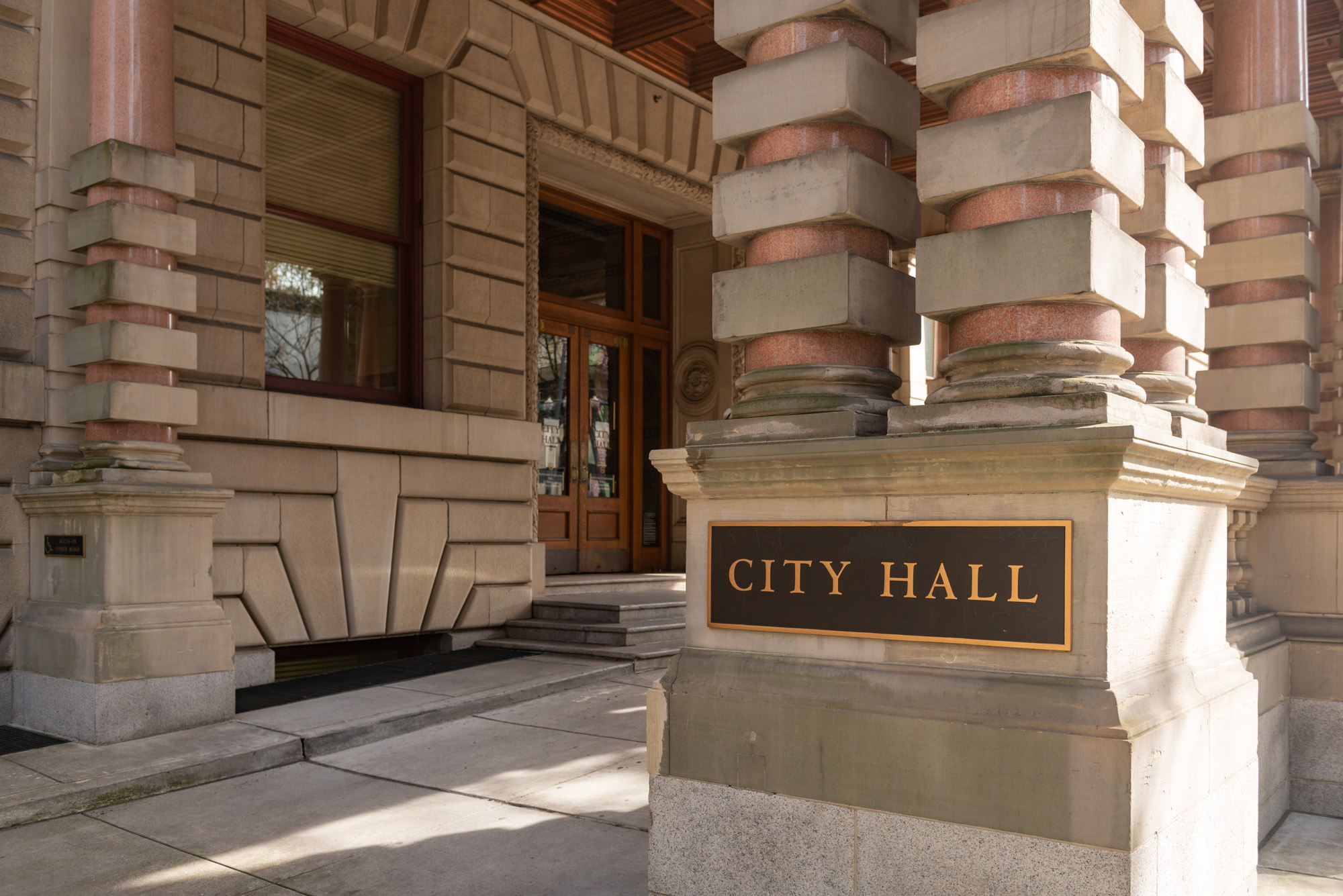 Stone entrance to a city hall building with a bronze sign reading 'City Hall.'