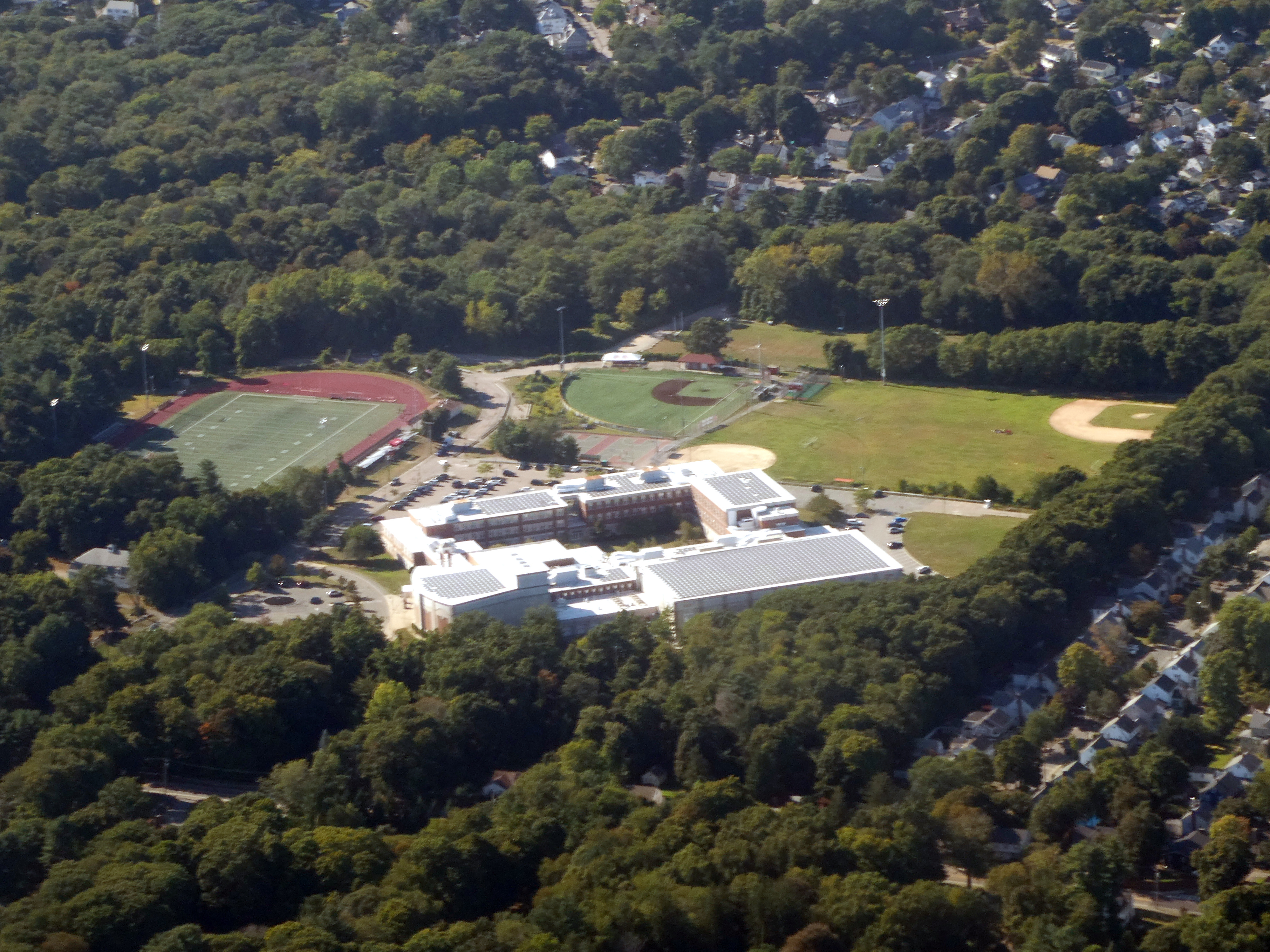 Aerial view of a school campus with a red running track and athletic fields surrounded by trees.
