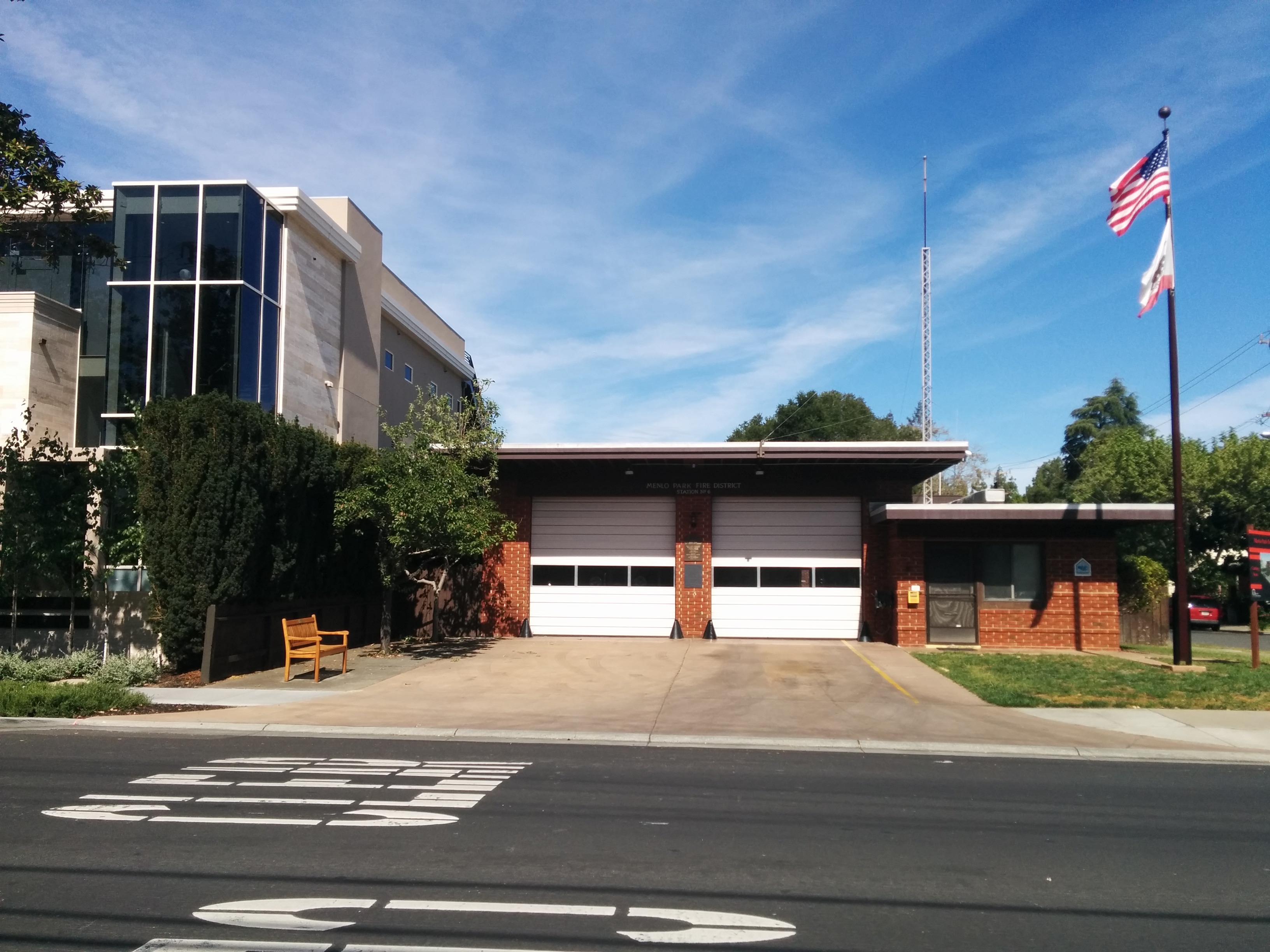 Single-story brick fire station with two white garage doors and flags on a pole.