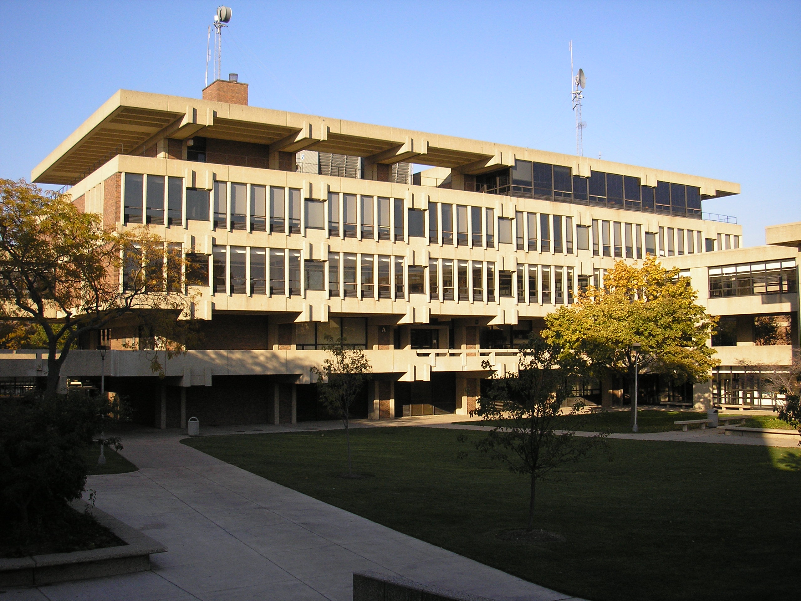 Multi-story brutalist-style school building with horizontal windows, surrounded by trees and walkways.