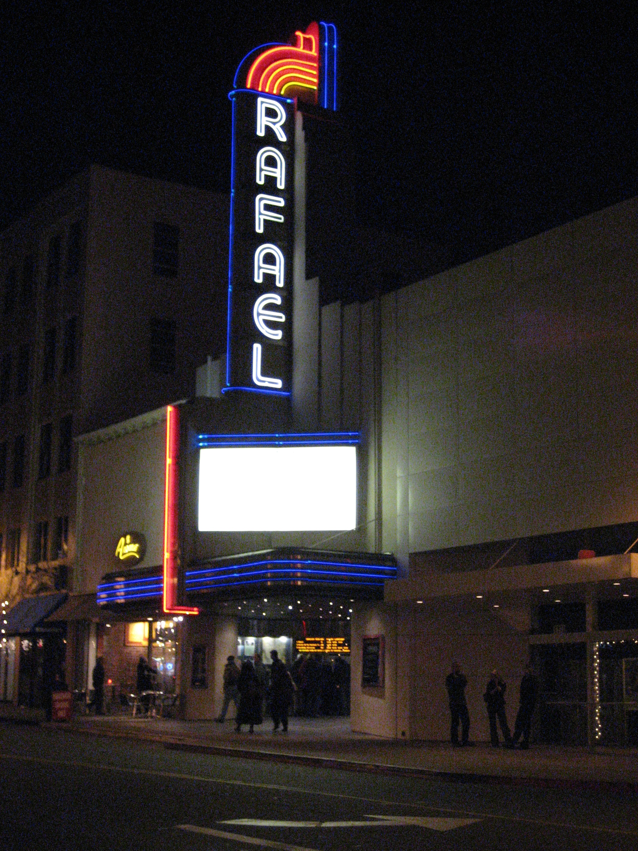 Theater with illuminated vertical neon sign and blue canopy lighting at night.