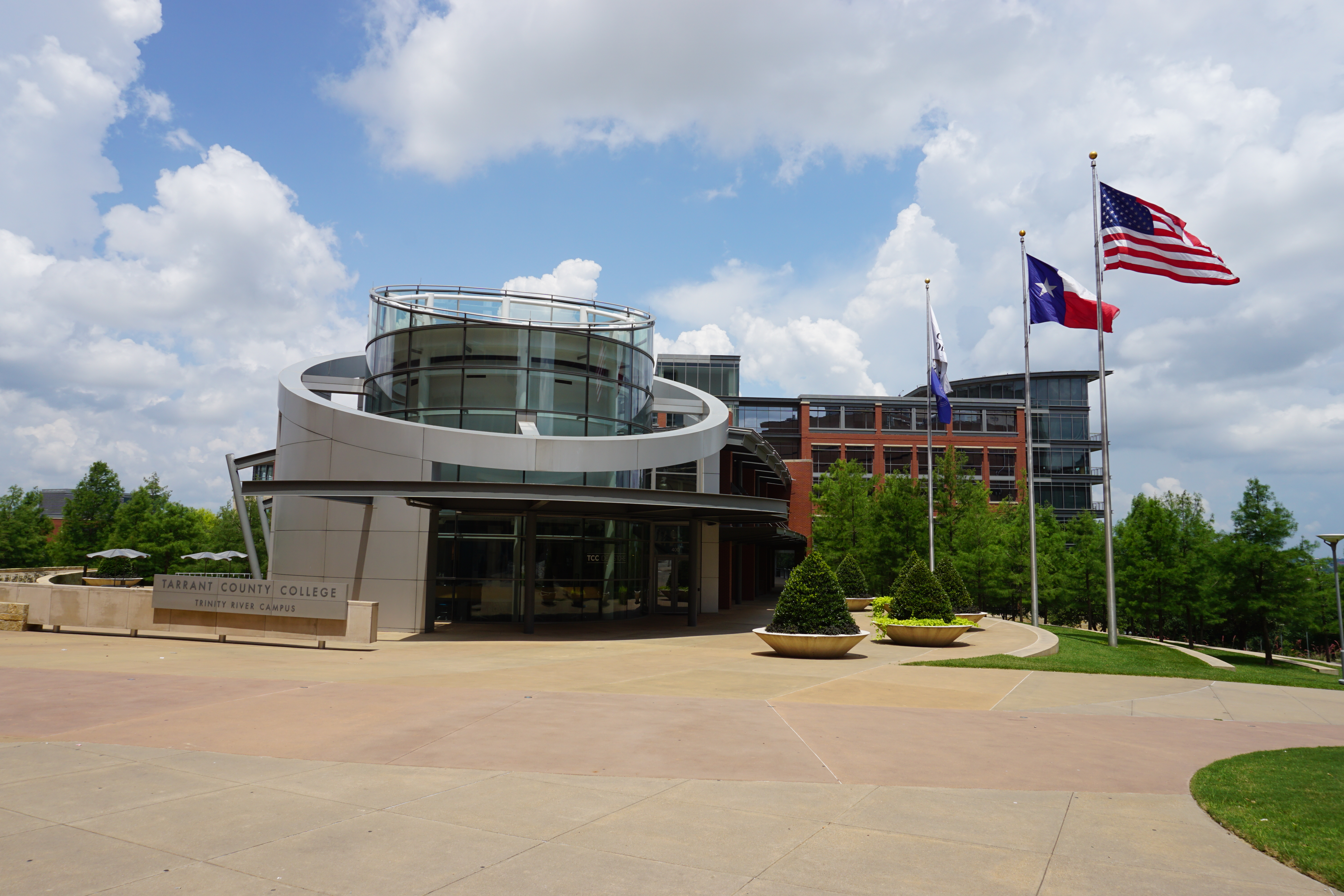 Modern curved glass rotunda building at a college campus with American and Texas flags.