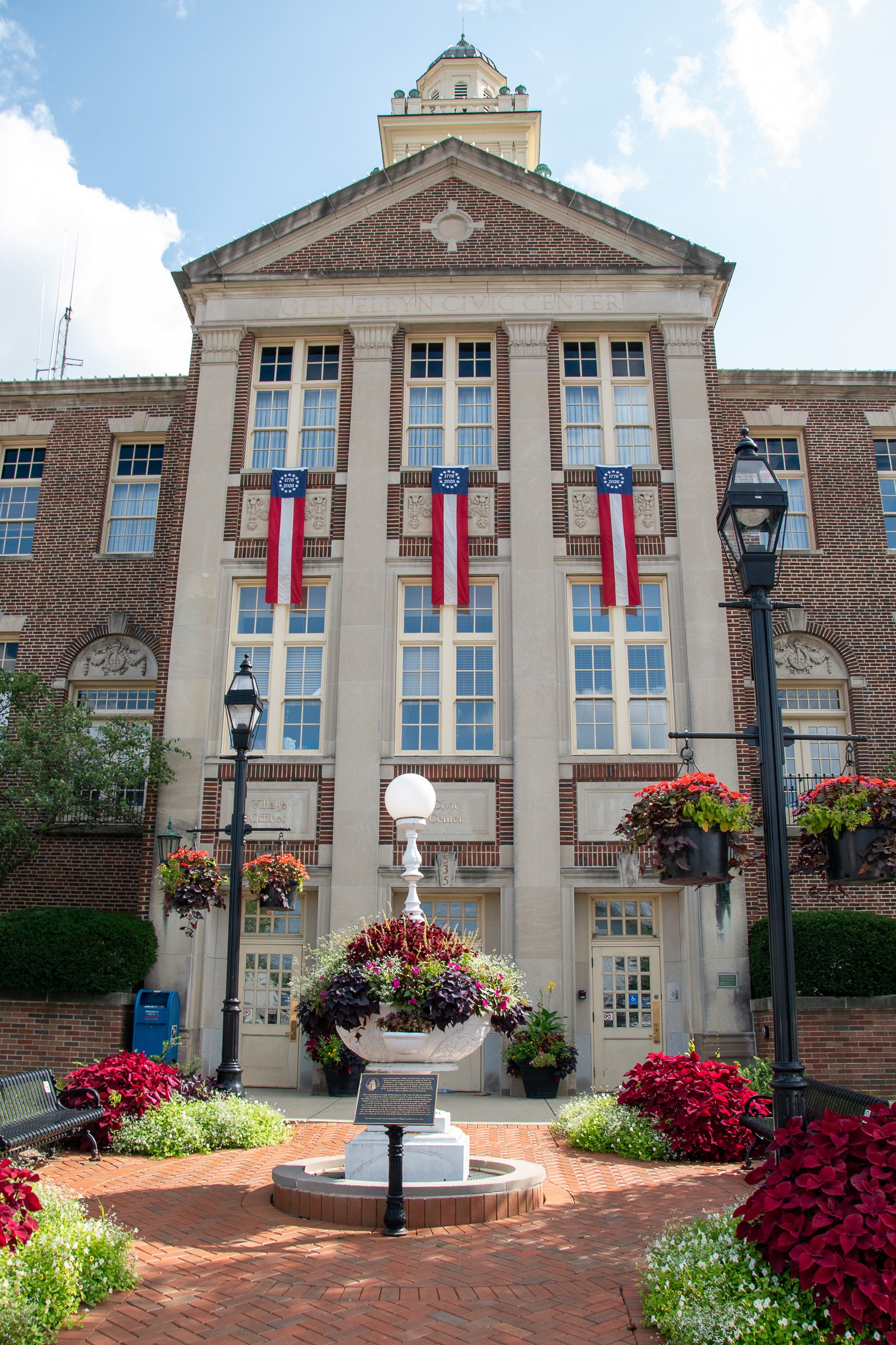 Red brick civic building with a green dome and decorative fountain plaza in front.