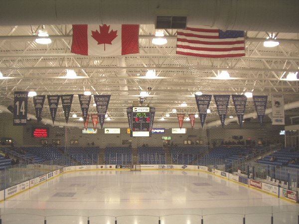 Empty ice rink inside an arena with championship banners and flags hanging from the ceiling.
