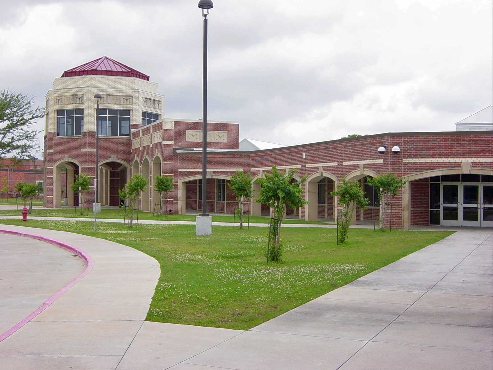 Red brick school building with arched entryways and a domed tower under a cloudy sky.