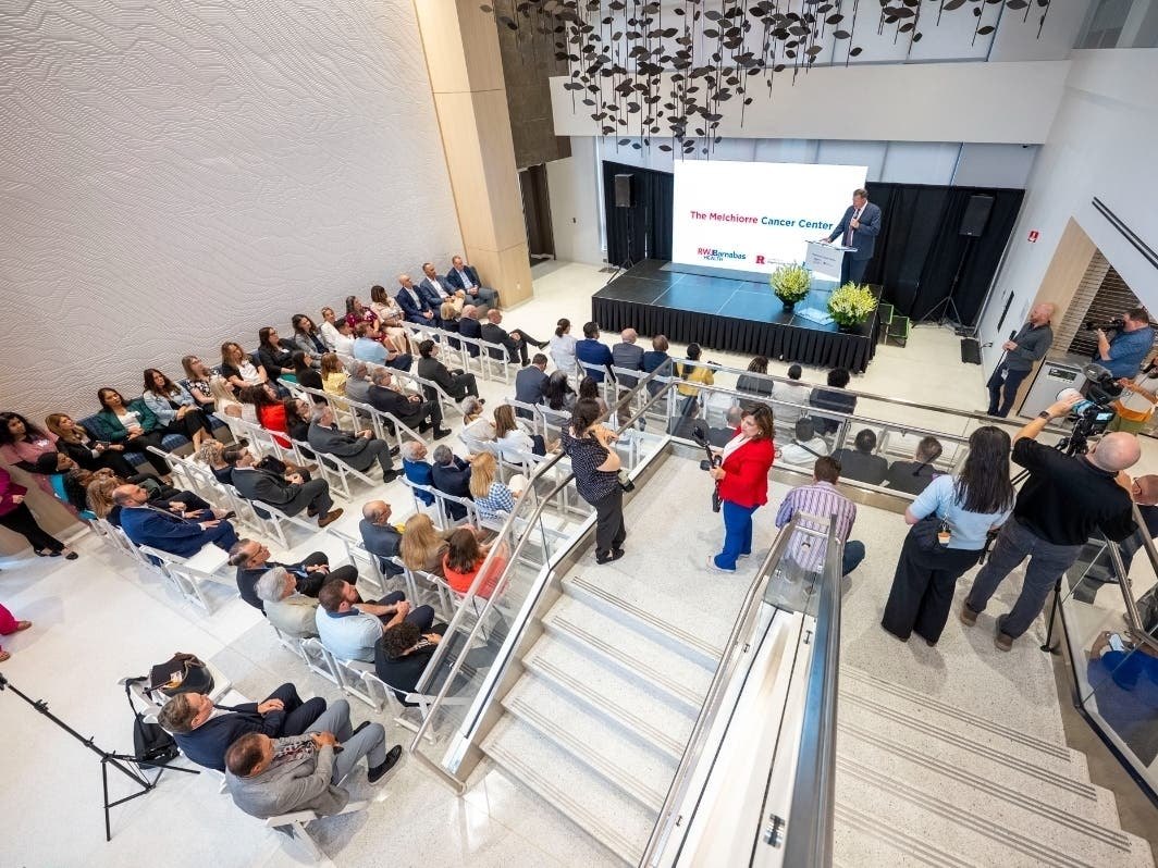 Overhead view of a presentation event in a modern atrium with audience seated in white chairs.