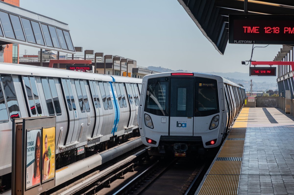 A BART train pulls into an outdoor elevated station platform.