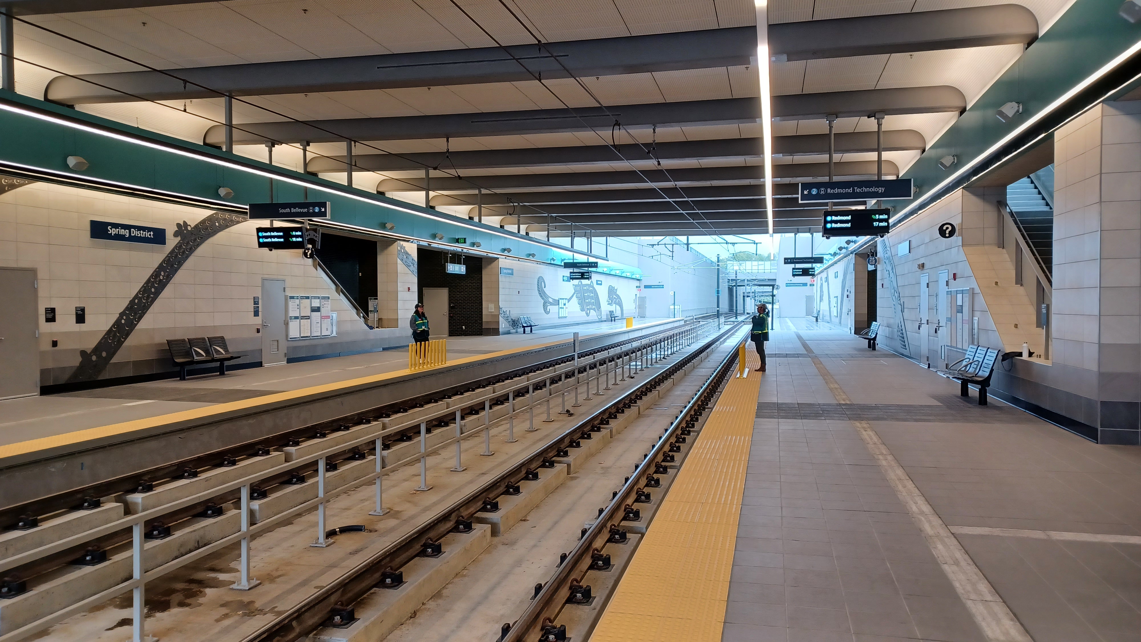 Empty light rail platform with dual tracks, yellow safety edge strips, and overhead signage.