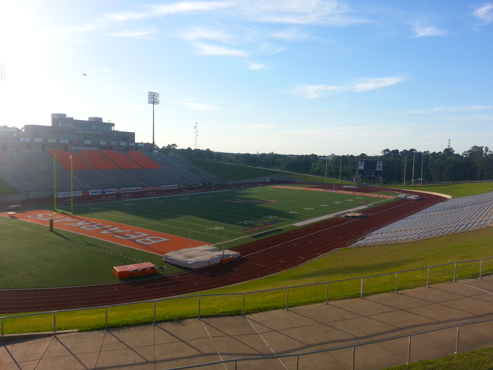 Empty college football stadium with orange seating, a running track, and green field.