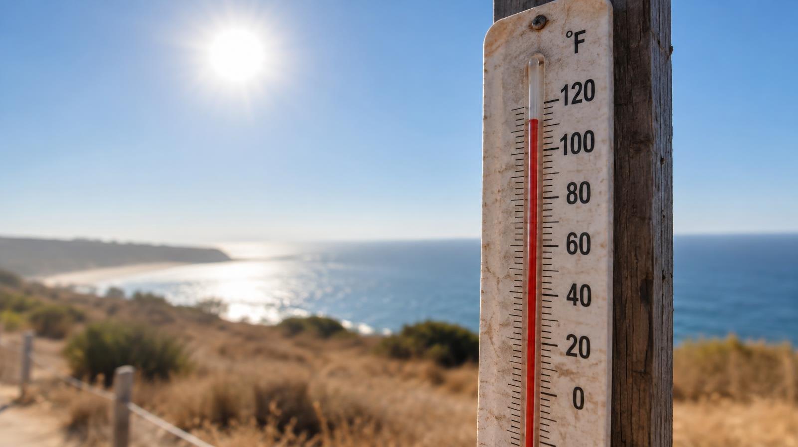 Outdoor thermometer on a post showing a high temperature under a bright sun.
