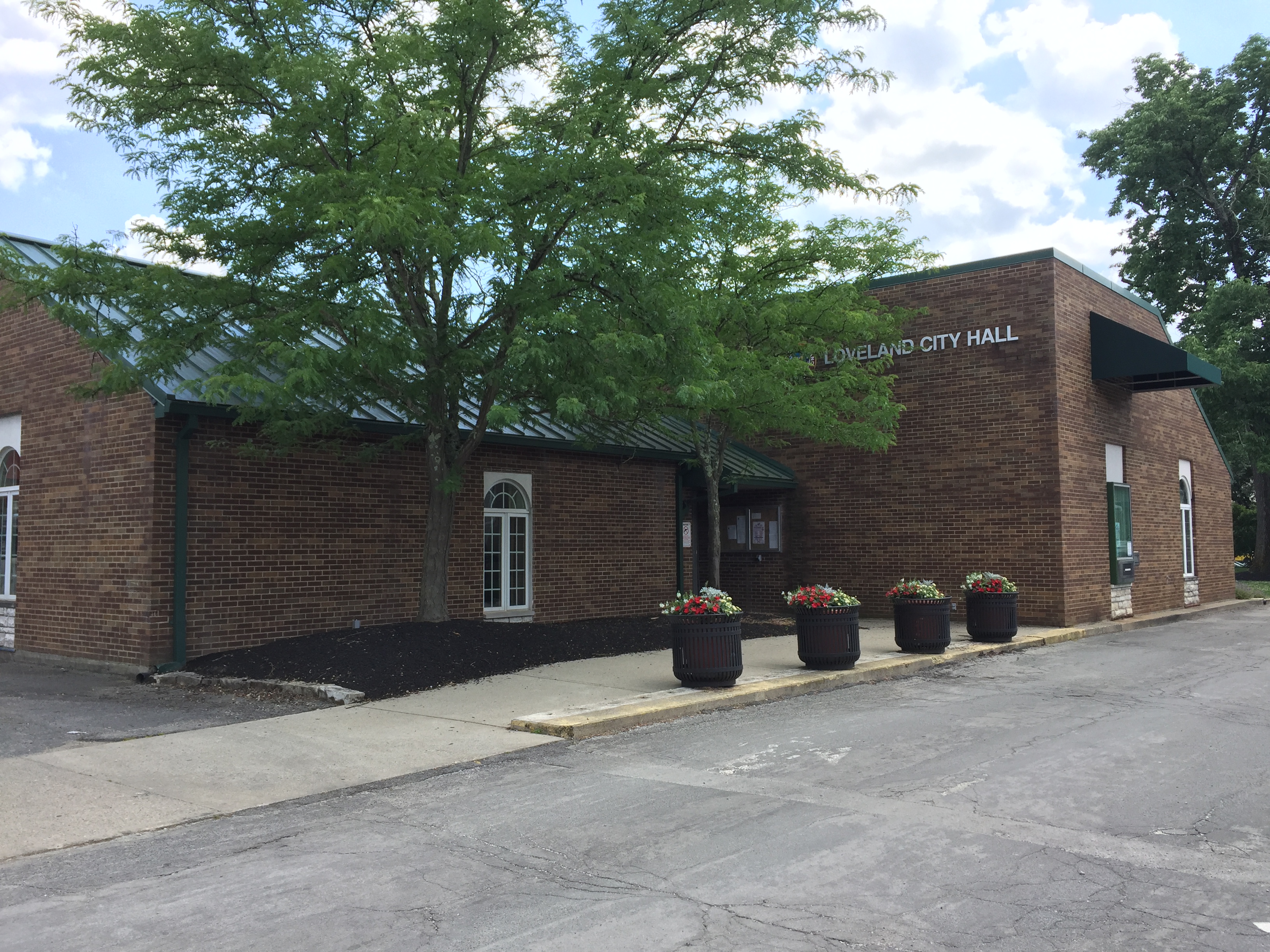 Exterior of a single-story brick municipal building with green awnings and flowering planters.