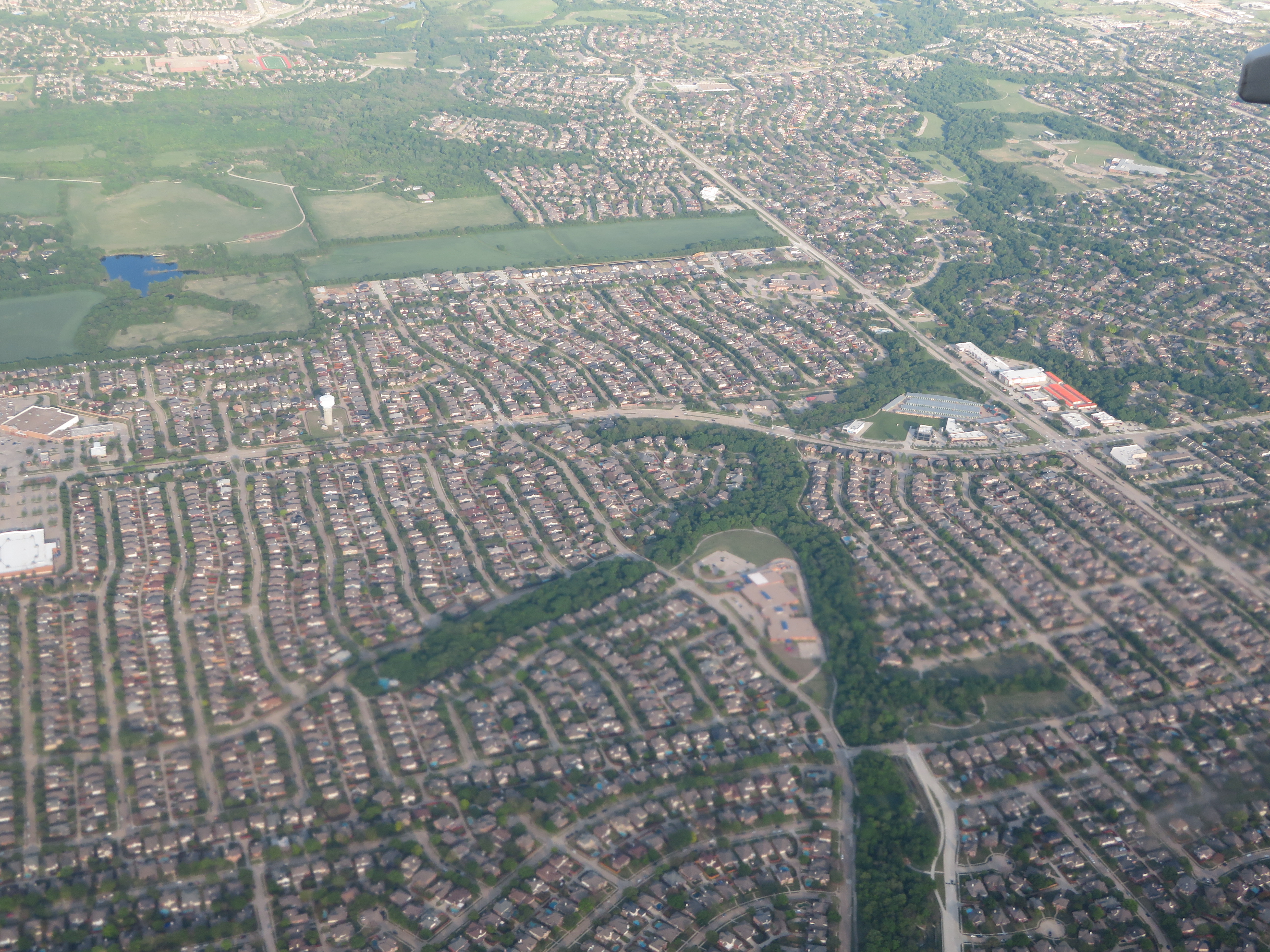 Aerial view of a dense suburban residential area with streets, houses, and green spaces.