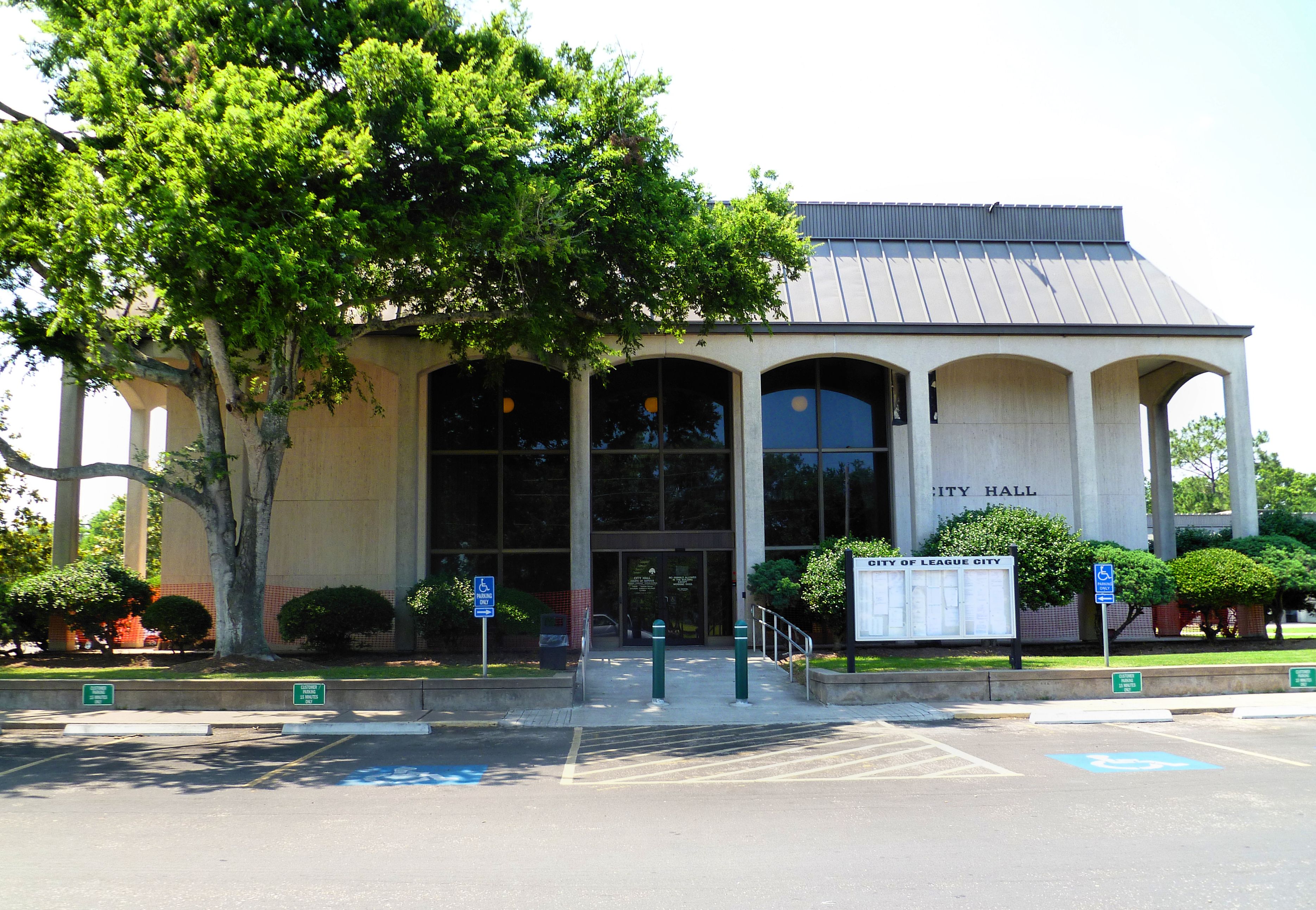 Municipal building with arched glass entrance, trees, and handicap-accessible parking in front.