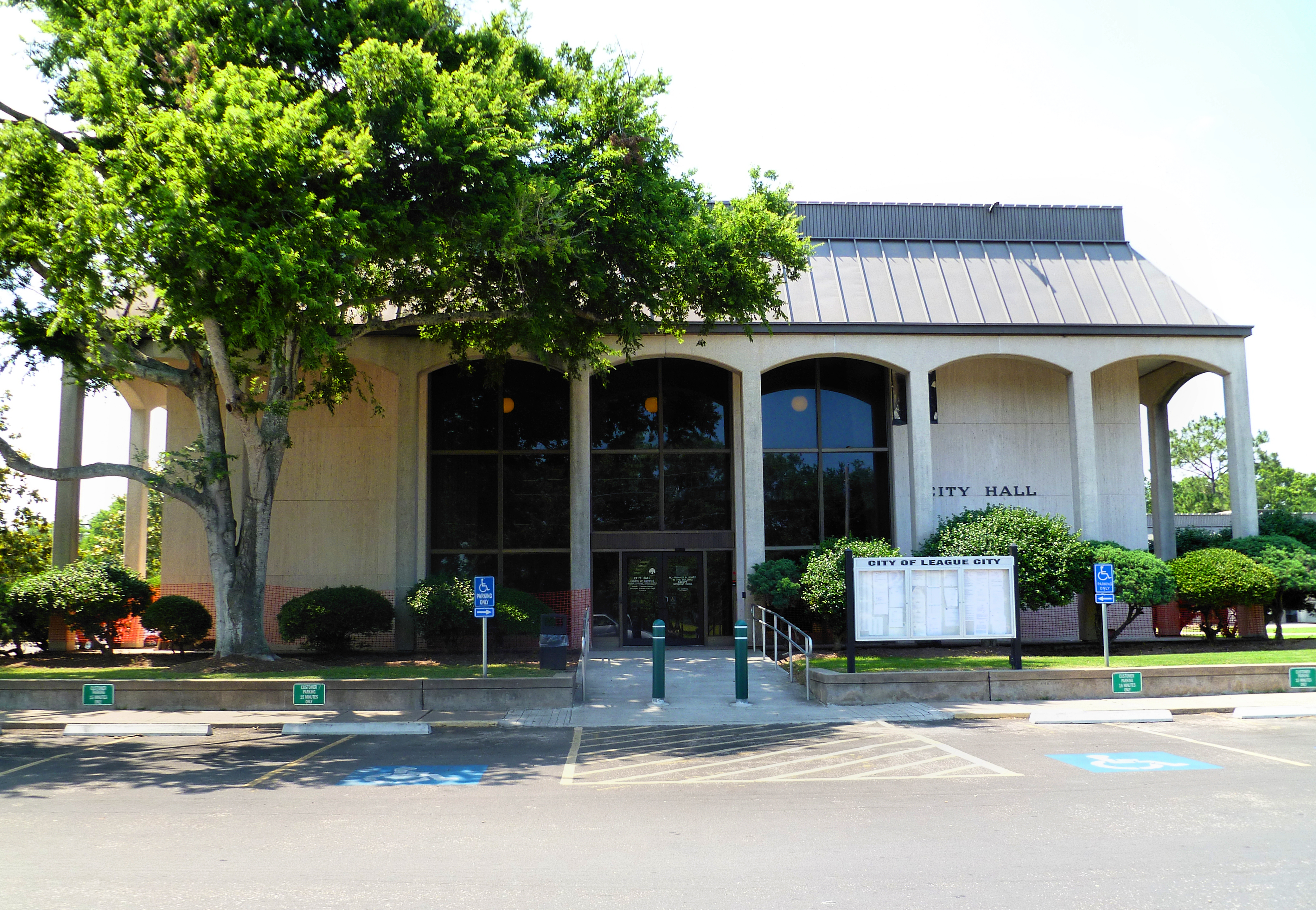 Municipal building with arched entryways, large trees, and a City Hall sign.